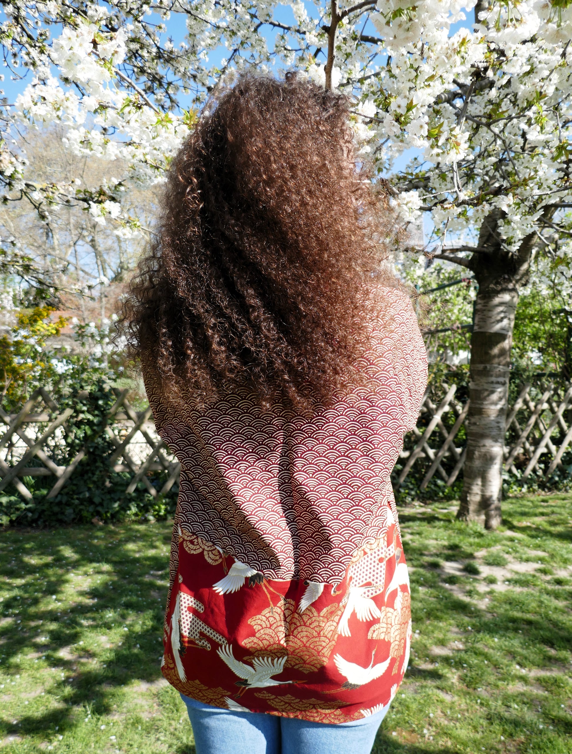 Haori Akane Tsuru vu de dos sur Loony, tissu traditionnel japonais rouge à motifs de grues et vagues seigaiha, en plein hanami.