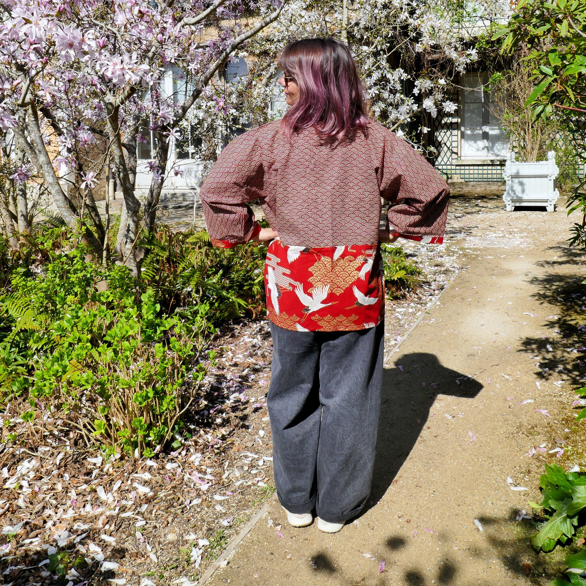 Vue de dos du haori Akane Tsuru porté par Mikan, révélant l’empiècement arrière avec grues et nuages dorés sur fond rouge vif.