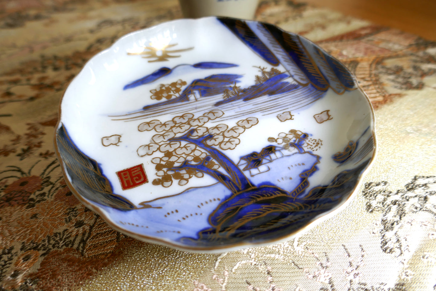 Gros plan sur le décor doré de paysage japonais et le sceau rouge Hizen sur assiette Meiji