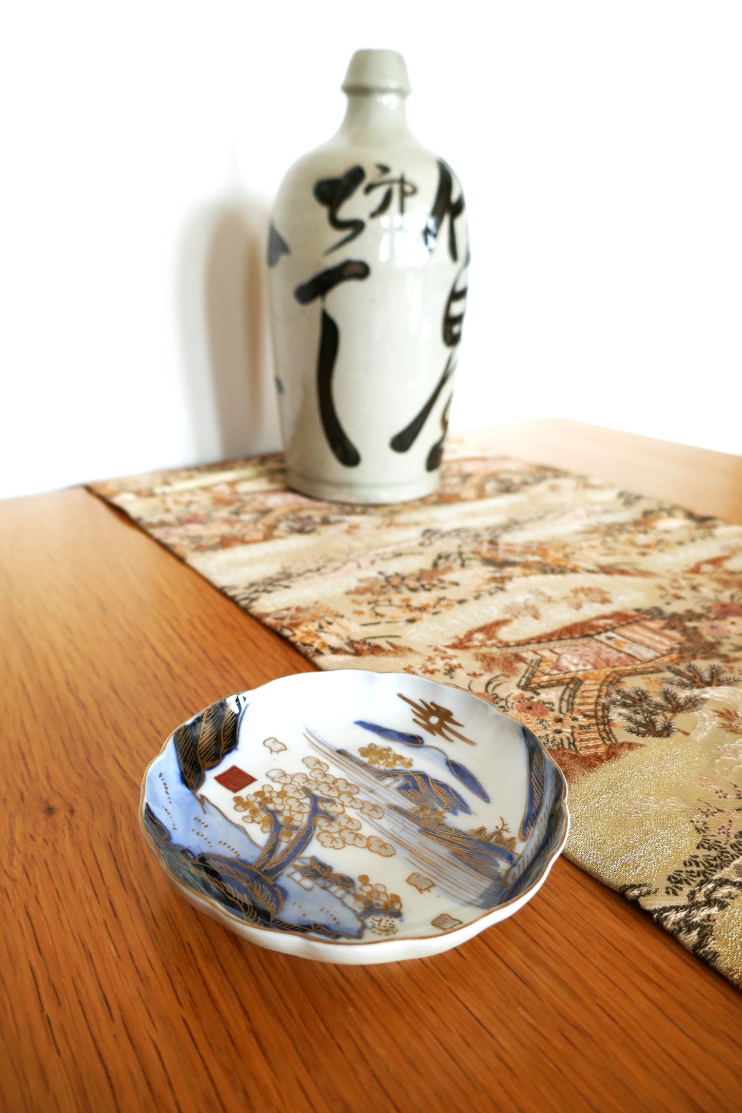 Présentation sur table d’une assiette japonaise Arita Meiji avec bouteille de saké artisanale