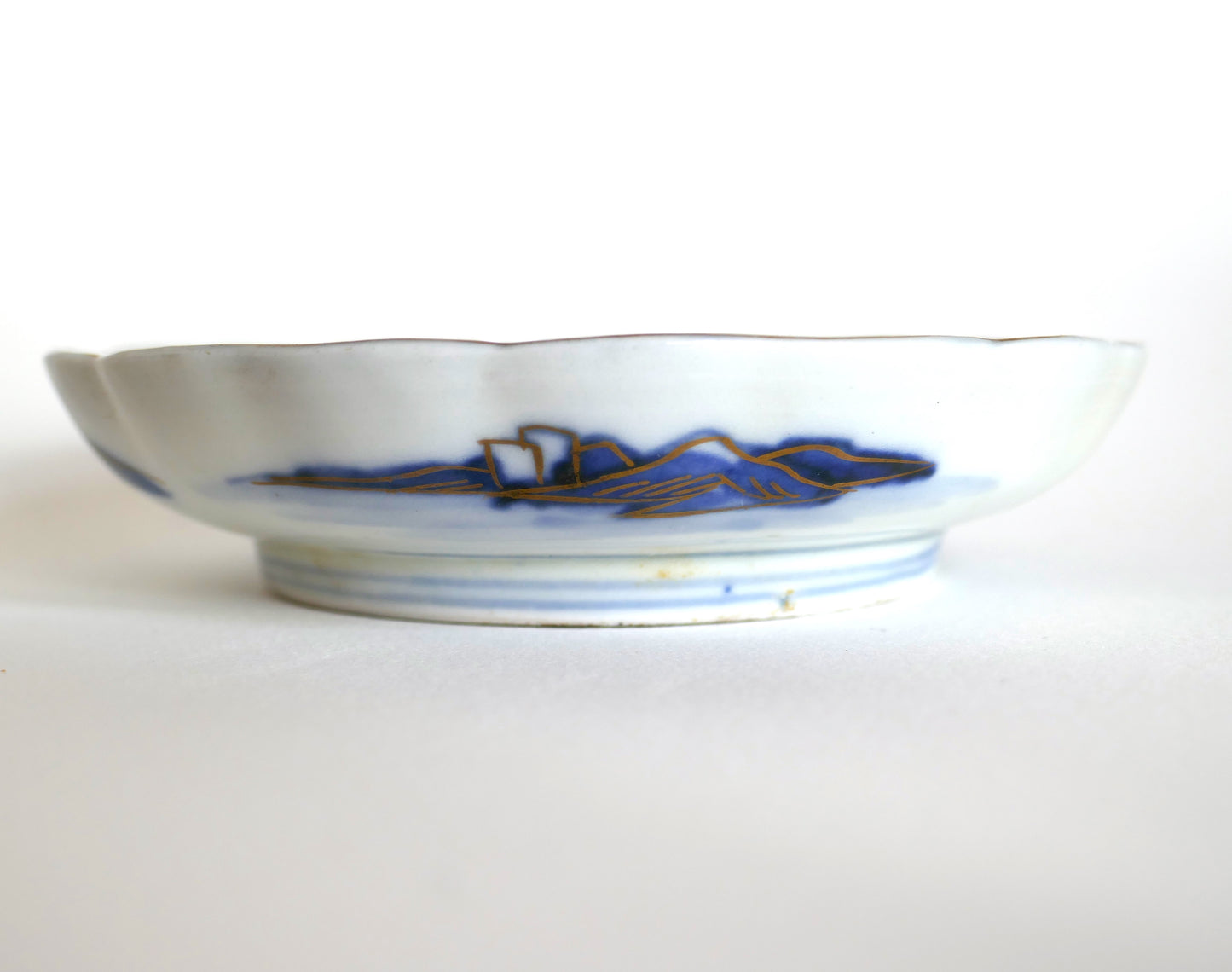 Vue latérale d’une assiette Arita Meiji montrant le décor extérieur de montagnes bleues et dorures