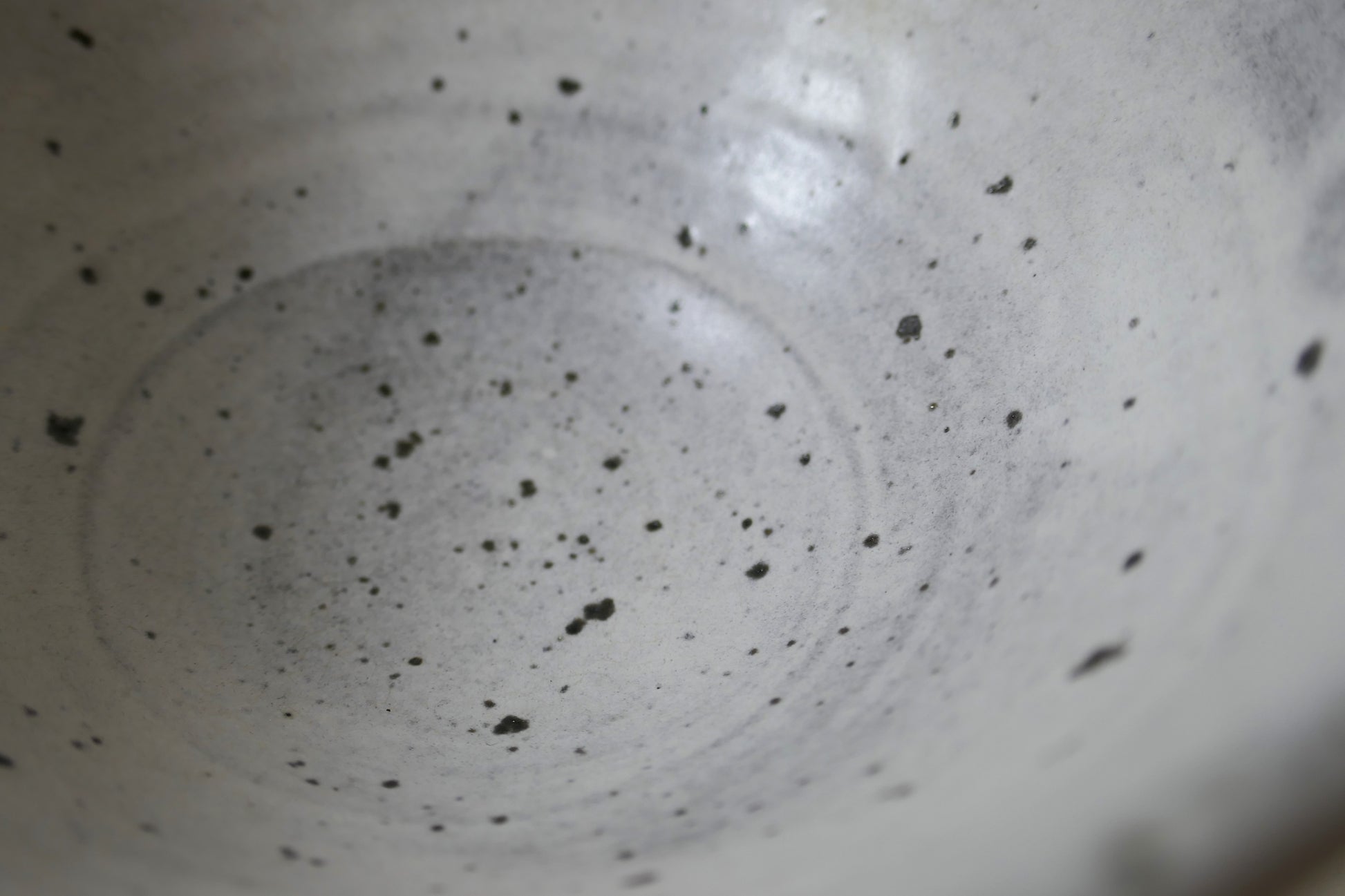Gros plan sur l'intérieur du chawan, glaçure blanche mate ponctuée de traces ferrugineuses révélées à la cuisson.