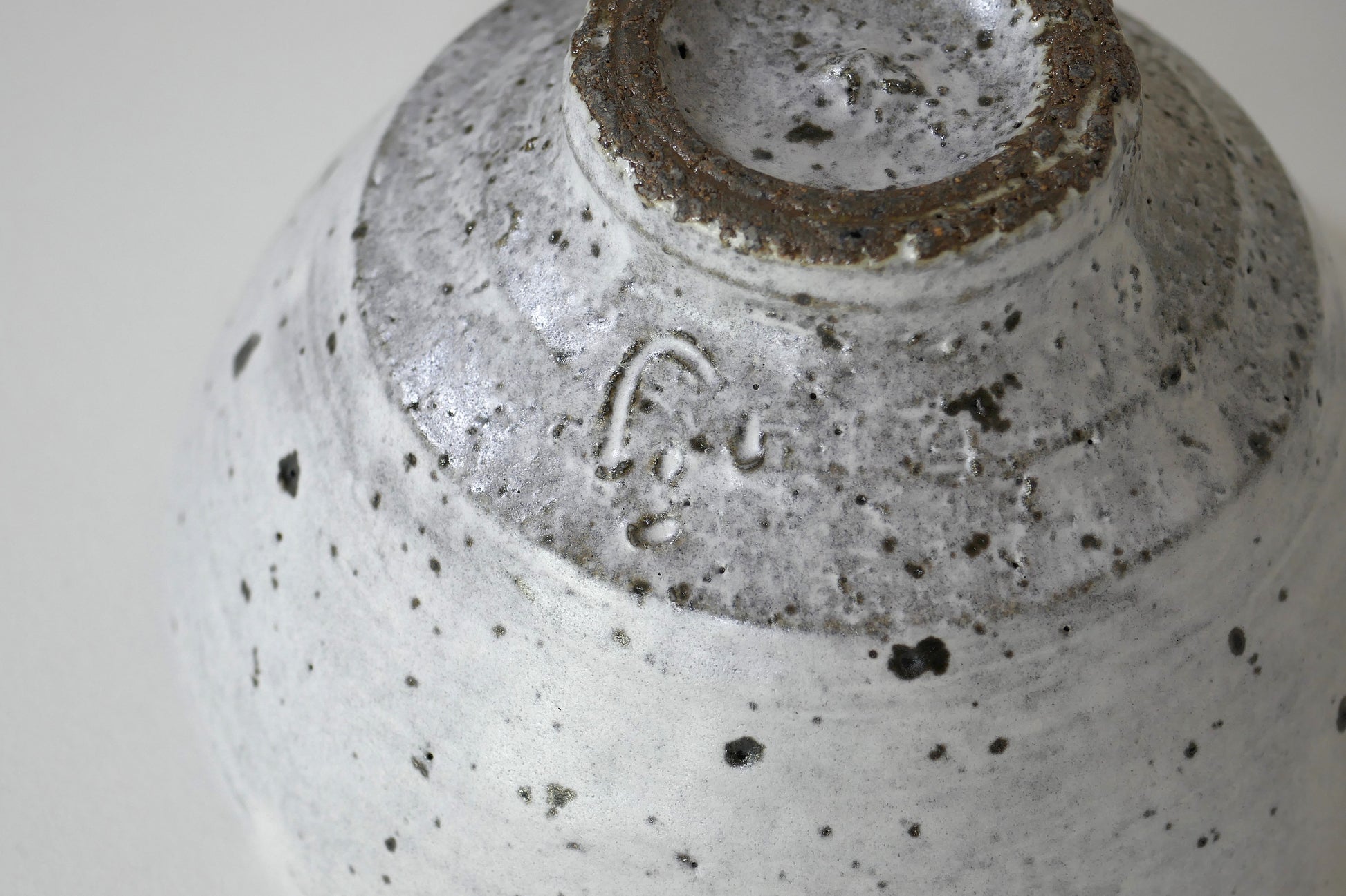 Détail en macro de la signature gravée sous le bol, glaçure fine laissant transparaître la texture du grès.