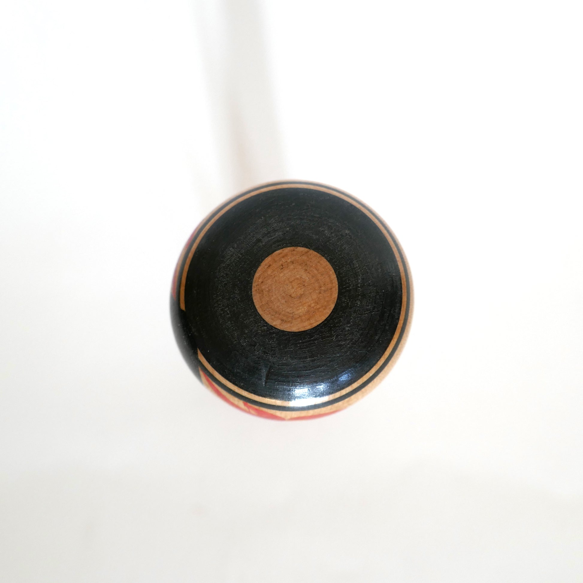 Vue du dessus de la tête d’une kokeshi Tsuchiyu présentant un motif Janome, dit œil de serpent rouge, typique de cette lignée artisanale.