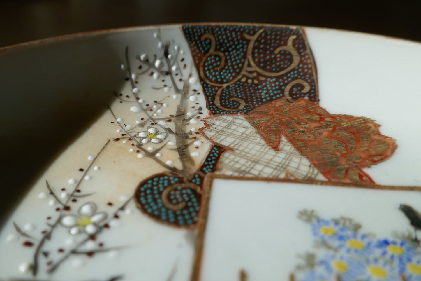 Détail des fleurs de prunier en émail blanc en relief et des motifs dorés sur assiette Kutani