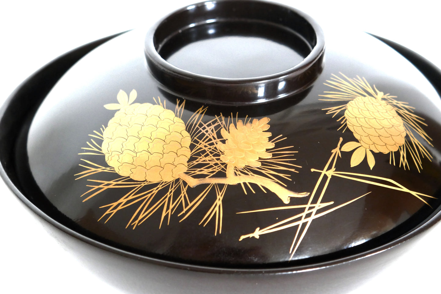 Détail du décor doré sur laque noire représentant des pommes de pin et des aiguilles – artisanat japonais raffiné