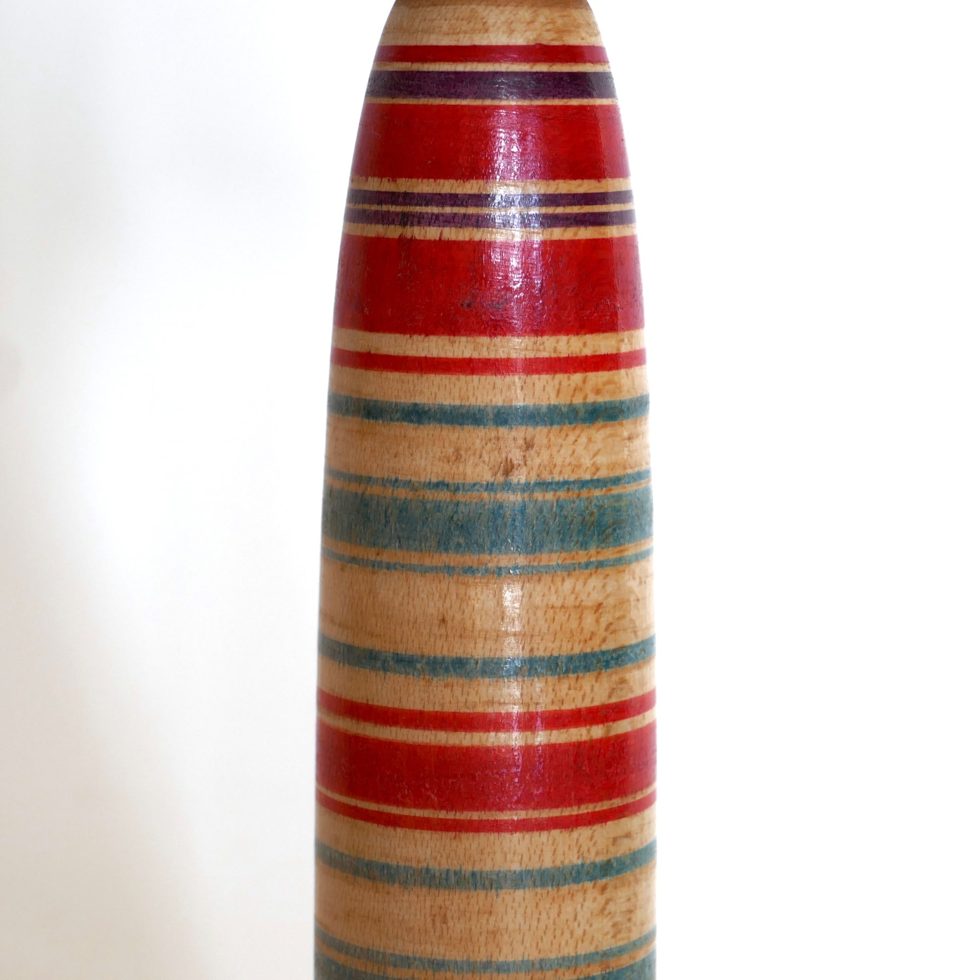 Détail du corps d’une kokeshi japonaise Tsuchiyu des années 1960, aux bandes peintes rouges, violettes et vertes caractéristiques.