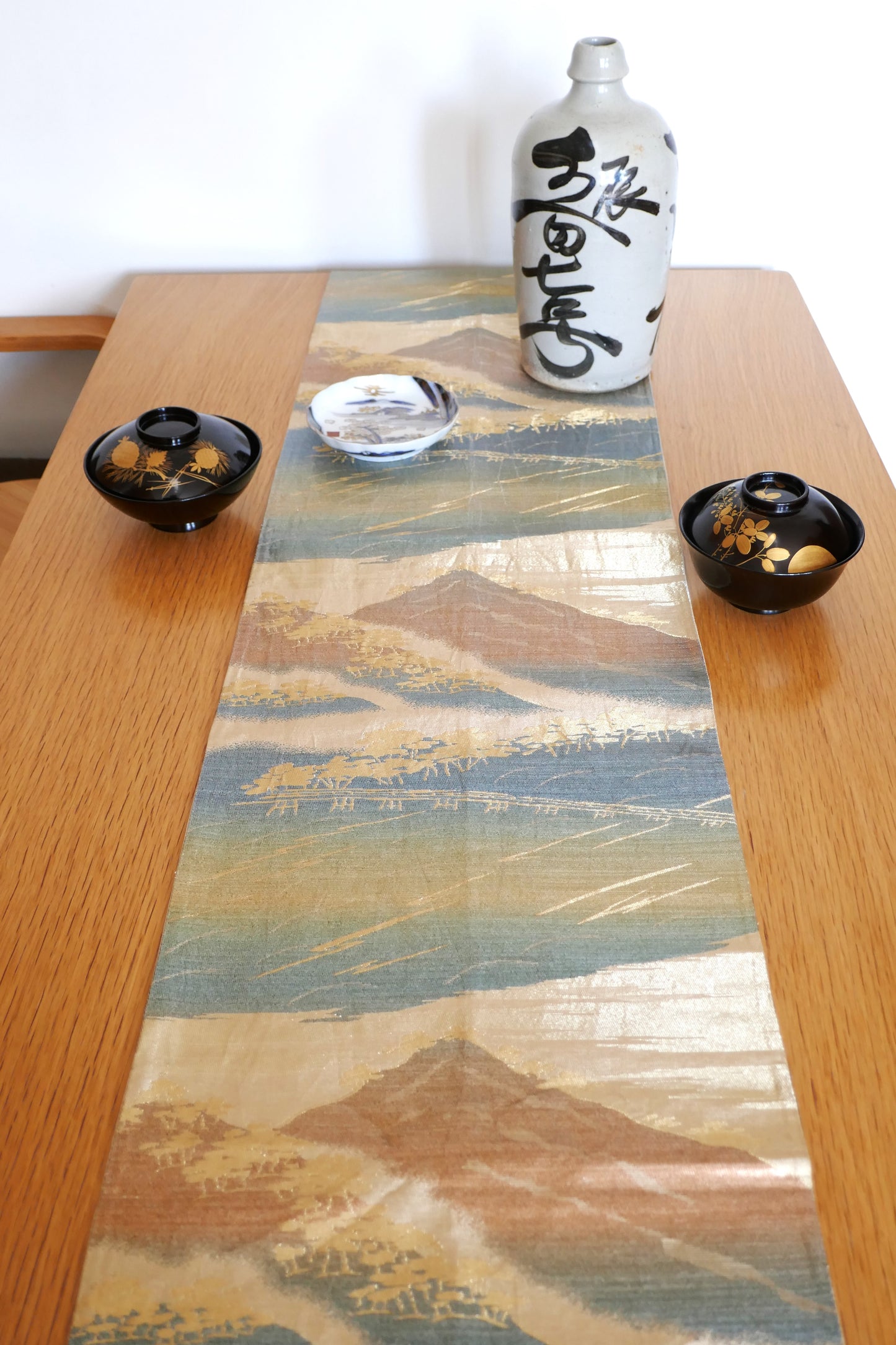 mise en scene sur une table à plat du fukuro obi Fuji KOGEDO avec des bols de laque une tokkuri et une assiette imari