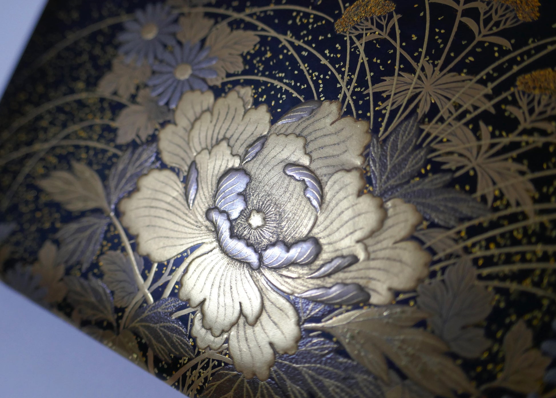 Gros plan sur pivoine dorée en maki-e sur boîte japonaise ancienne, œuvre de l’atelier Zohiko à Kyoto.