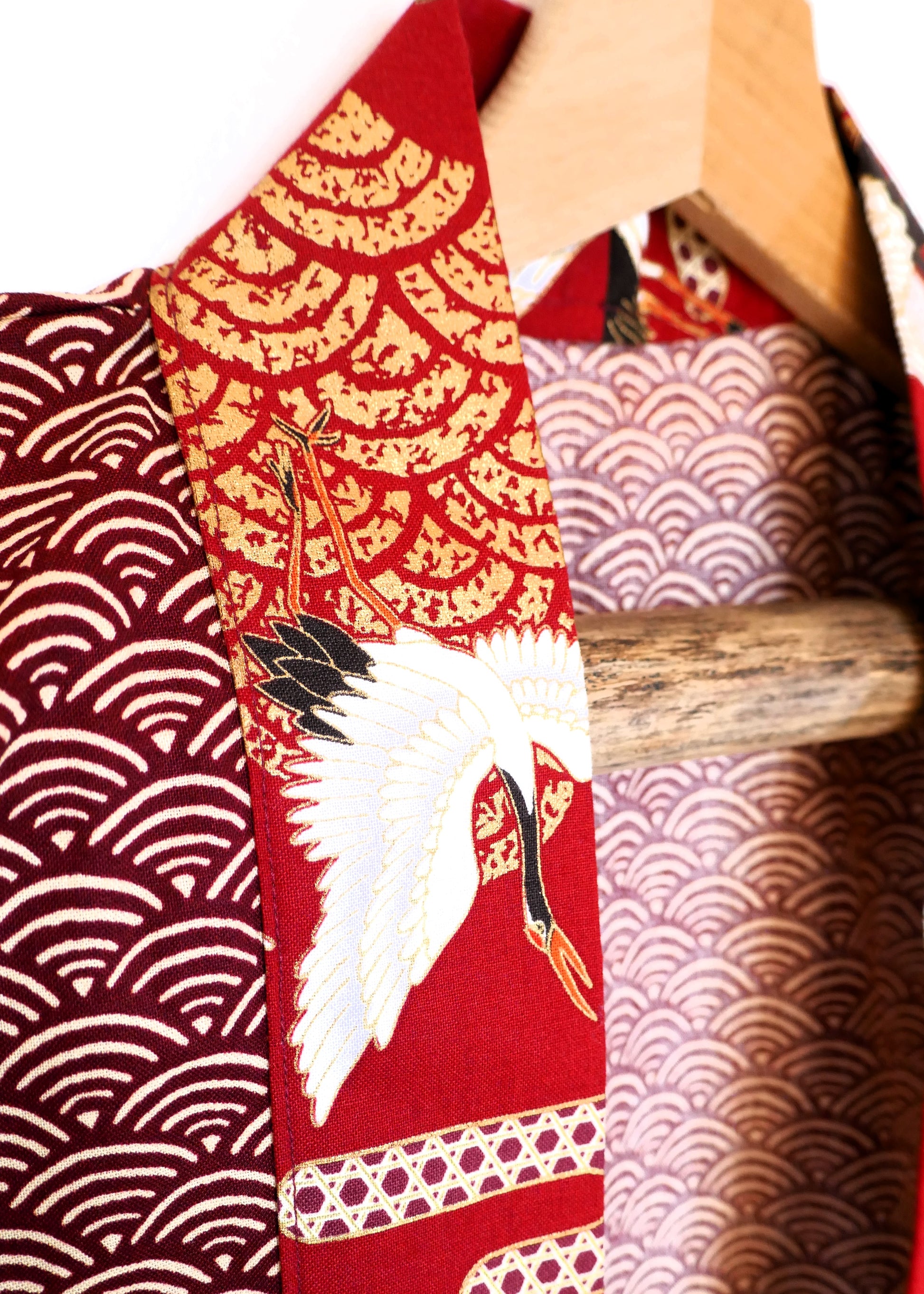 Gros plan sur le col du haori Akane Tsuru, avec tissu rouge carmin orné d’une grue blanche et de nuages dorés stylisés et de vagues dorées seigaiha