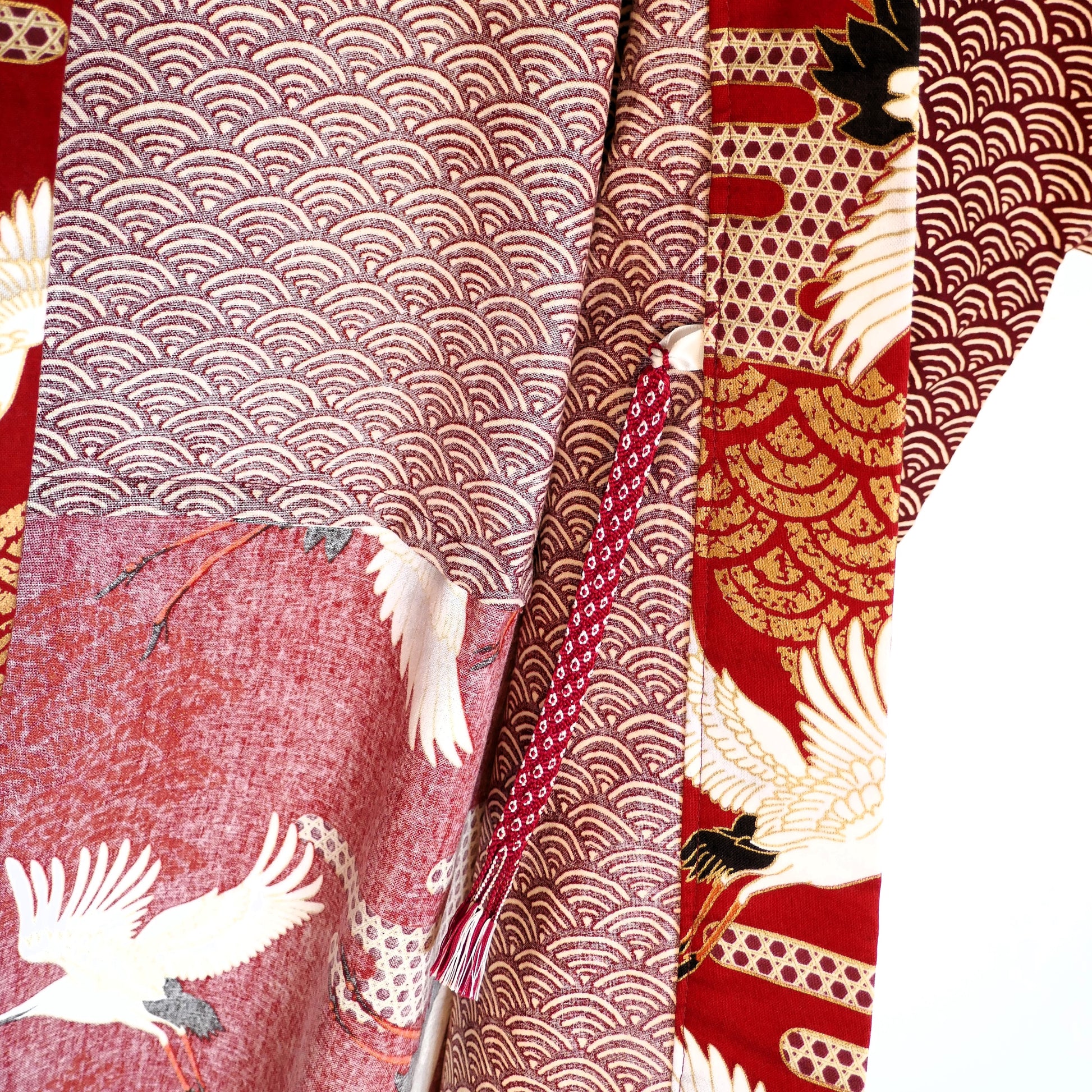 Détail du lien de fermeture du haori Akane Tsuru, noué sur fond rouge à motifs de vagues et grues blanches en plein vol.