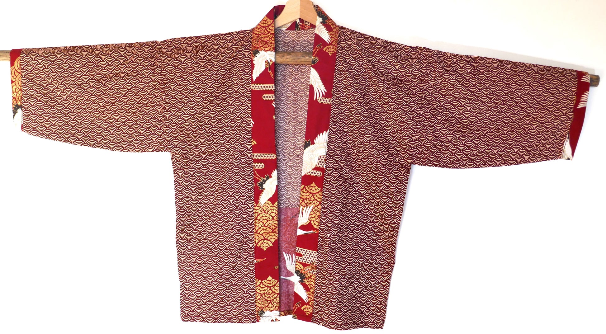 Vue de face du haori japonais Akane Tsuru suspendu, col en tissu contrasté à motifs de grues blanches et fond seigaiha rouge.