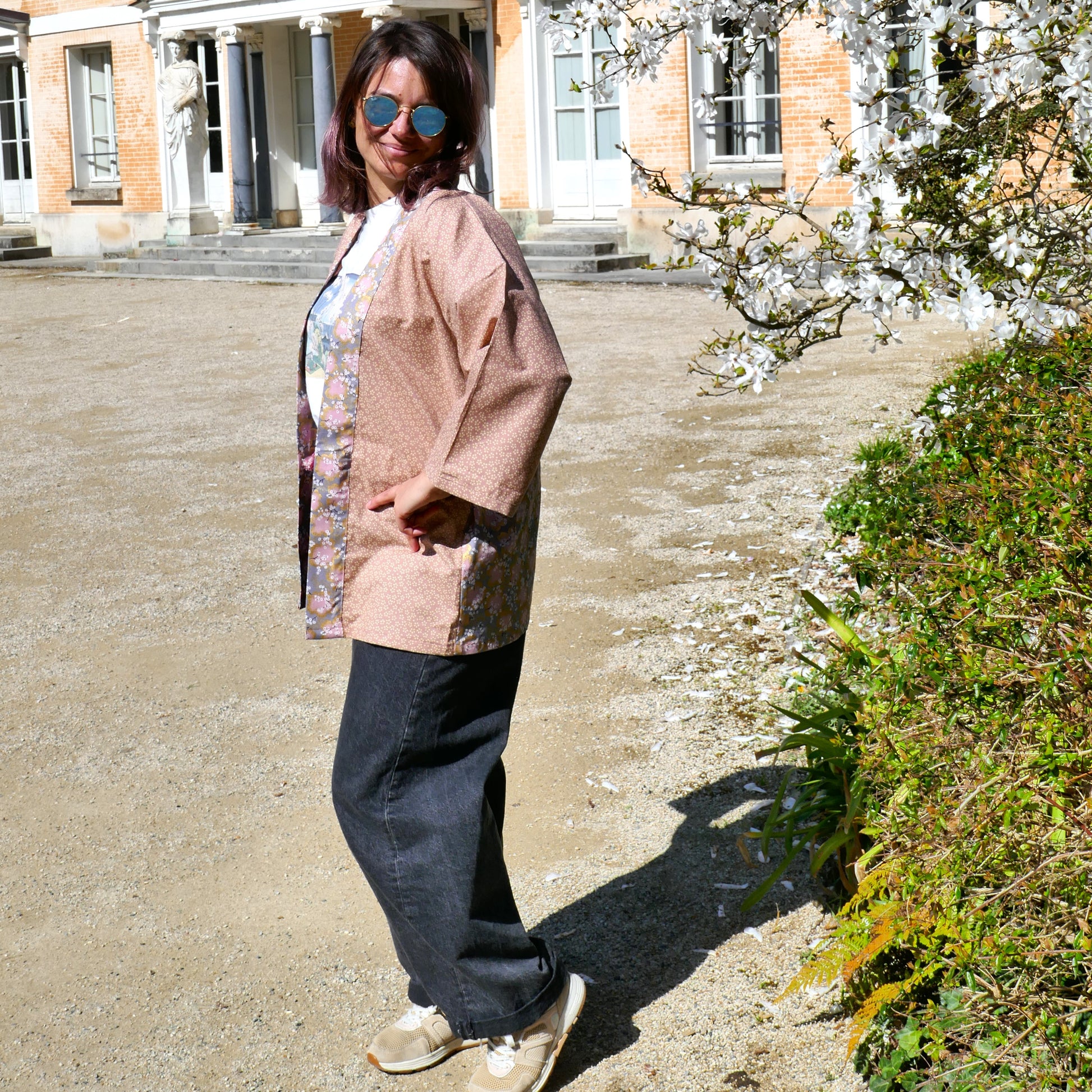 Mikan porte le haori Hanami devant un magnolia en fleurs, soulignant ses motifs sakura vieux rose – look printanier et décontracté.