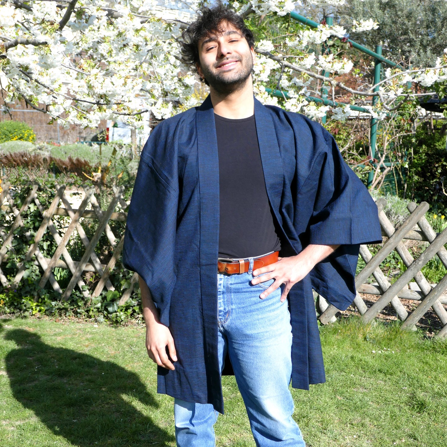 Richard porte un haori homme en laine bleu marine, debout dans un jardin fleuri au printemps.