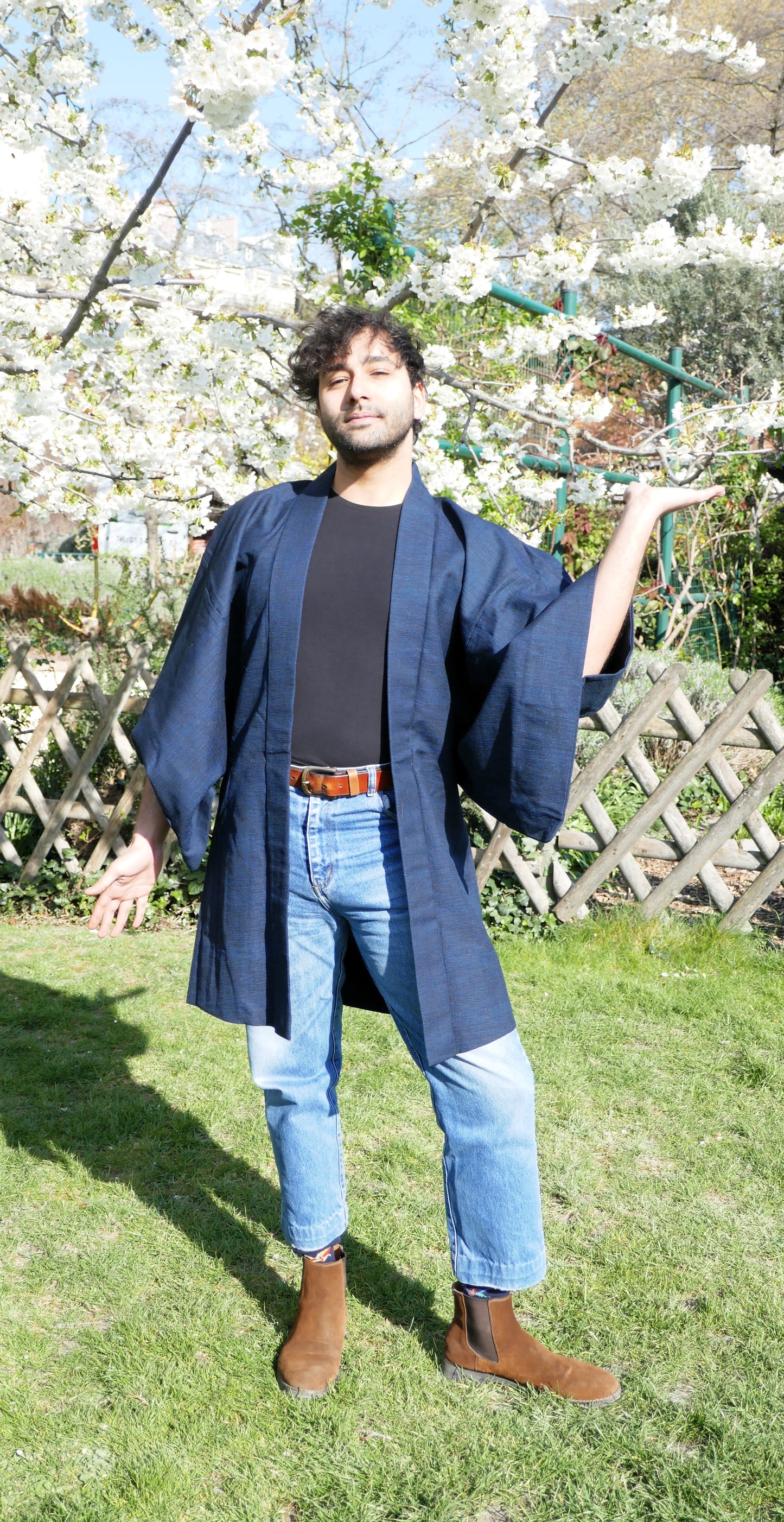 Haori homme porté par Richard, en jean et t-shirt noir, pose décontractée sous les cerisiers en fleurs.