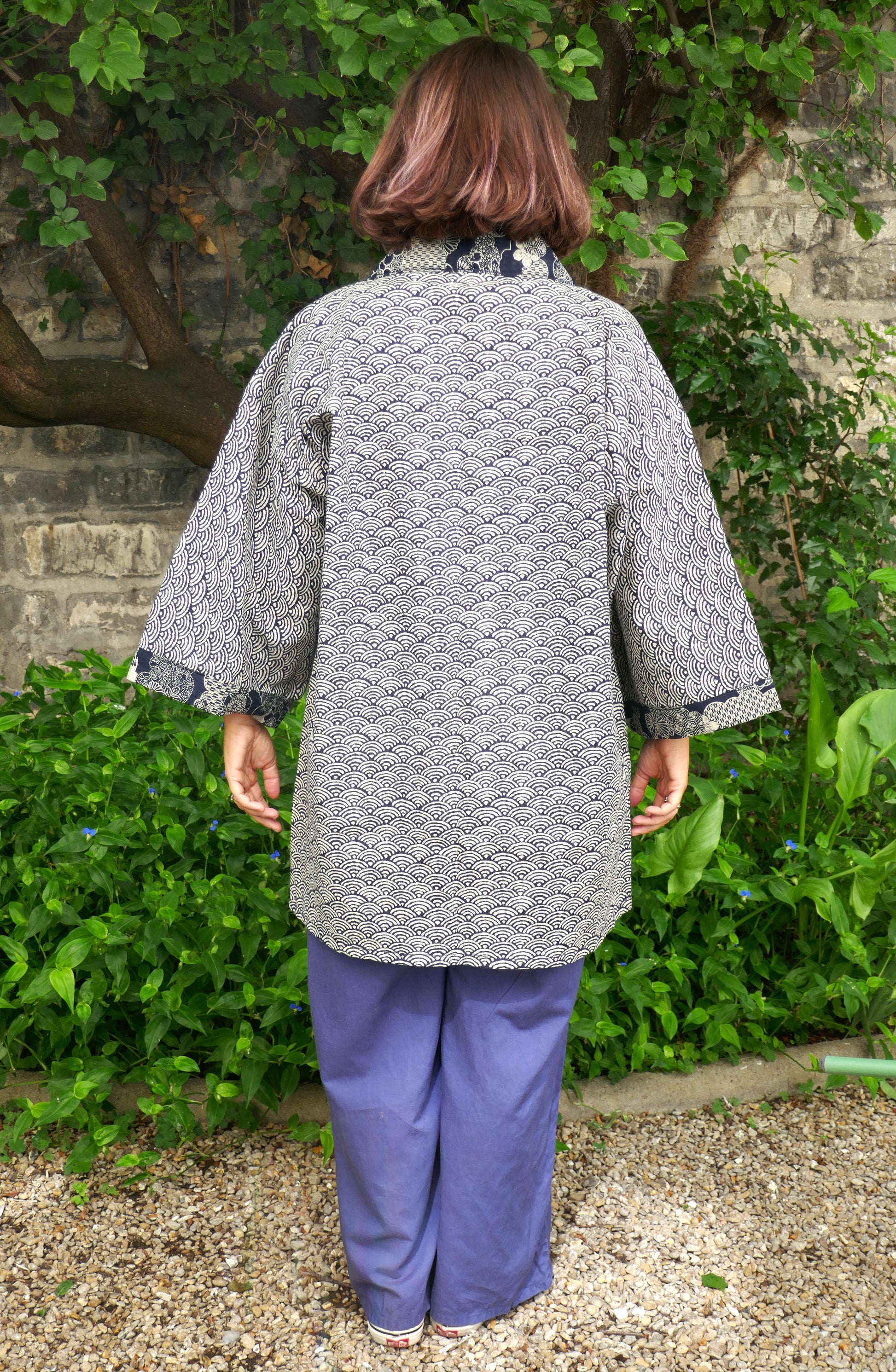 Mikan portant un haori kimono moderne de l’atelier KOGEDO, modèle “Umi no Sakura”, vu de dos. Motif traditionnel japonais seigaiha (vagues) en bleu et blanc, col et poignets ornés de fleurs de cerisier. Style zen et épuré.