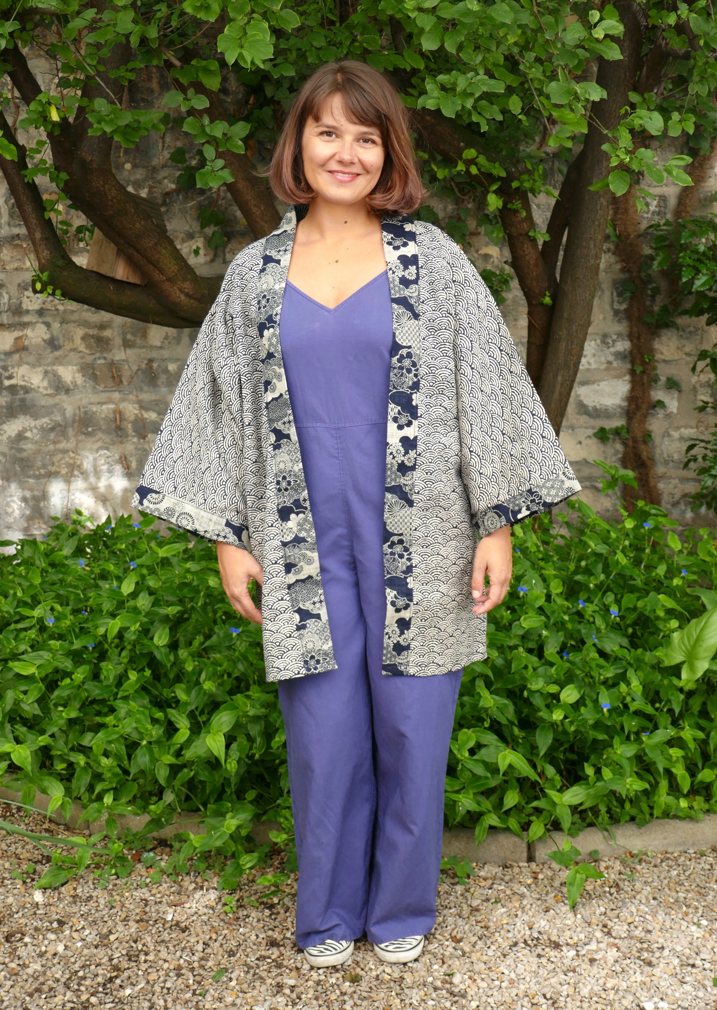 Mikan souriante dans le haori “Umi no Sakura” signé KOGEDO, veste kimono moderne à imprimé vagues japonaises seigaiha, bordures à motifs floraux sakura en bleu nuit. Tenue japonaise contemporaine et féminine dans un jardin verdoyant.