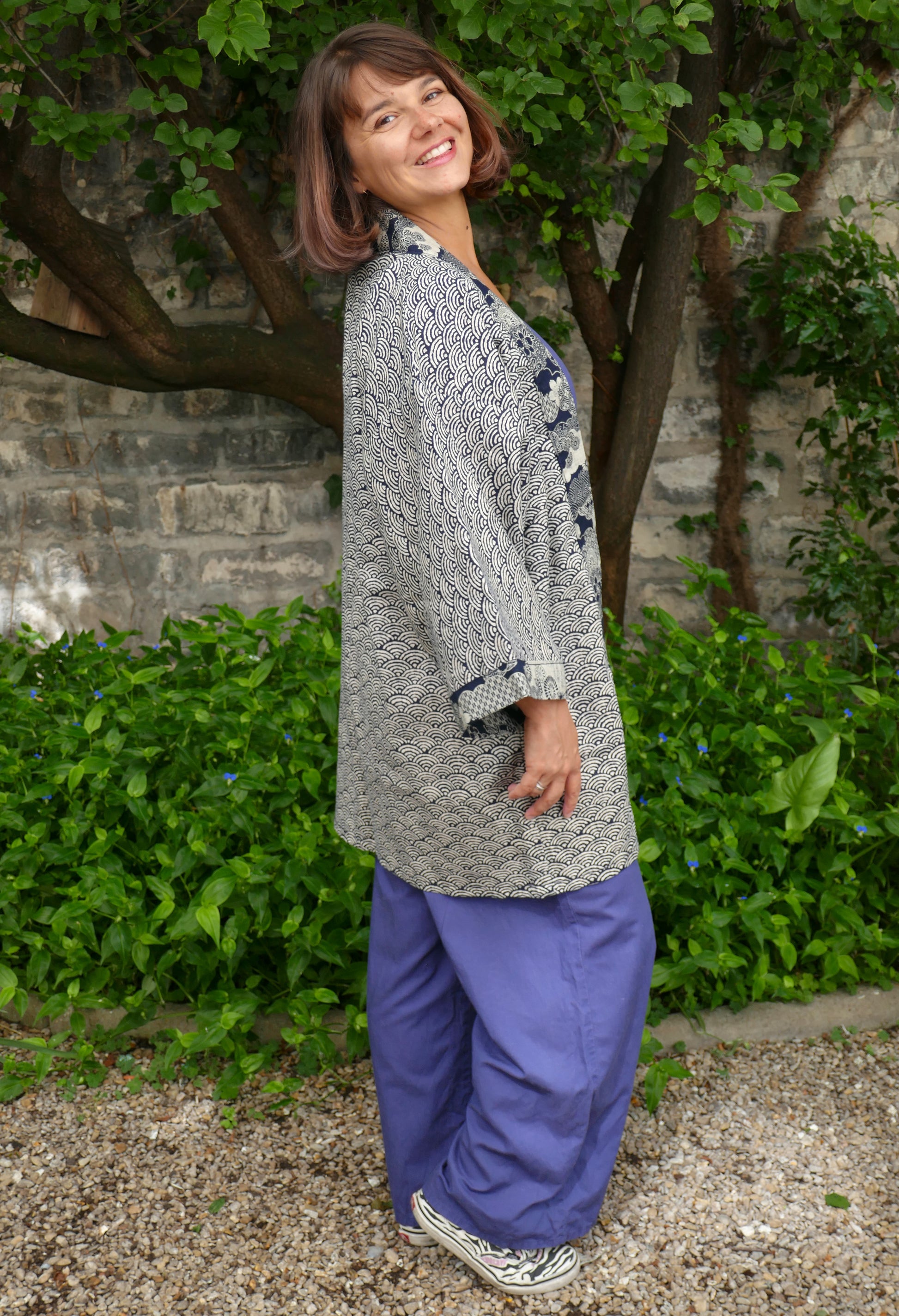 Vue de profil de Mikan dans le haori japonais “Umi no Sakura”. Motifs seigaiha élégants, tissus japonais de qualité avec finitions florales. Veste kimono moderne au style poétique et graphique.