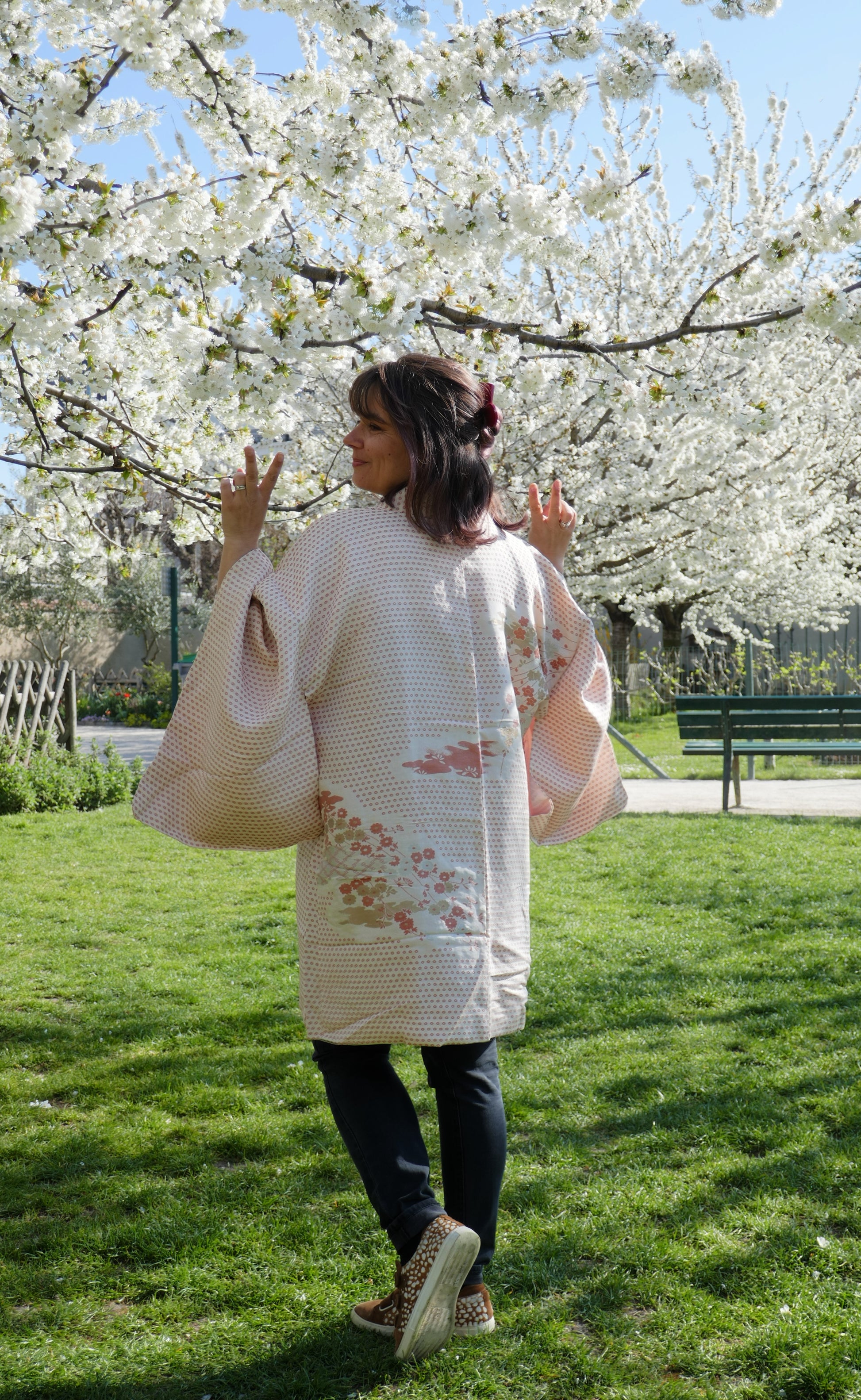 Haori vintage japonais à motifs de prunier (ume) porté par Mikan, vue de dos sous les cerisiers en fleurs.