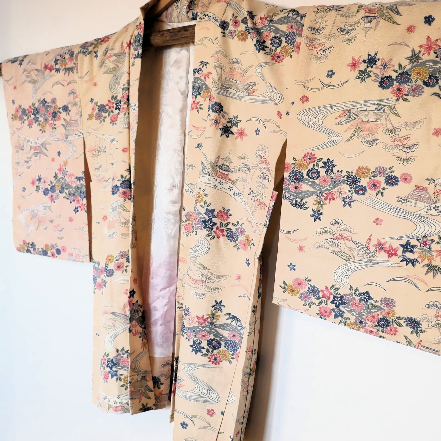 Vue de trois-quarts du haori vintage suspendu, montrant son motif de rivières et fleurs colorées sur fond ivoire