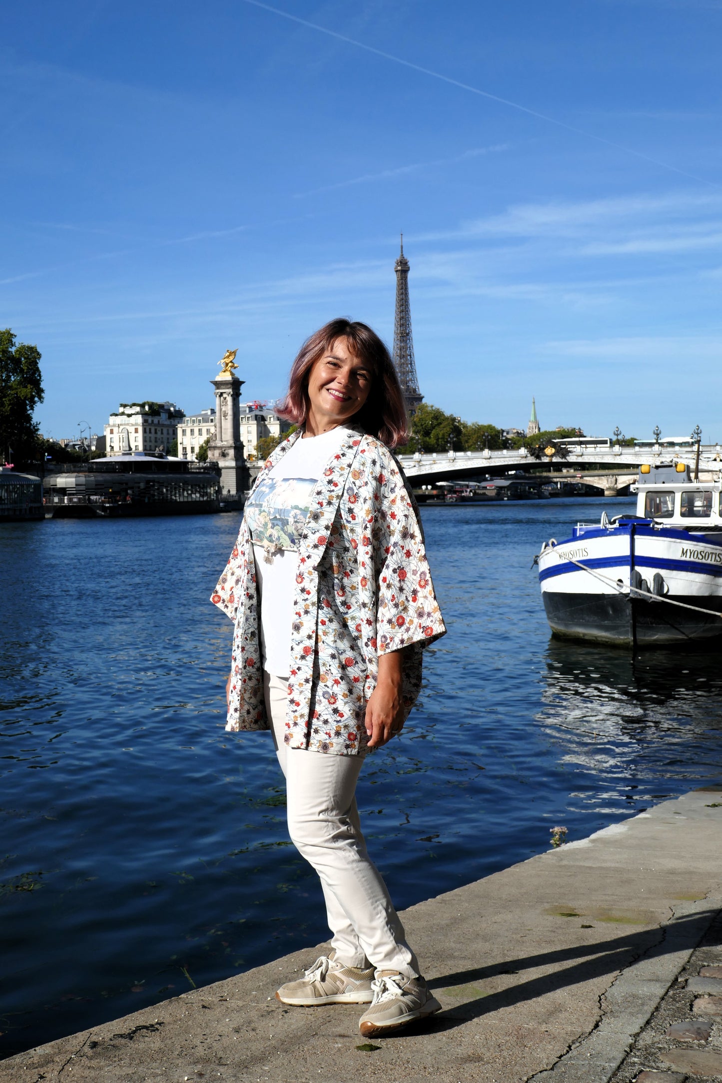 Mikan souriante en veste kimono traditionnelle haori vintage japonais en soie, motif chrysanthèmes 菊 et érables rouges 紅葉, près de la Seine à Paris.