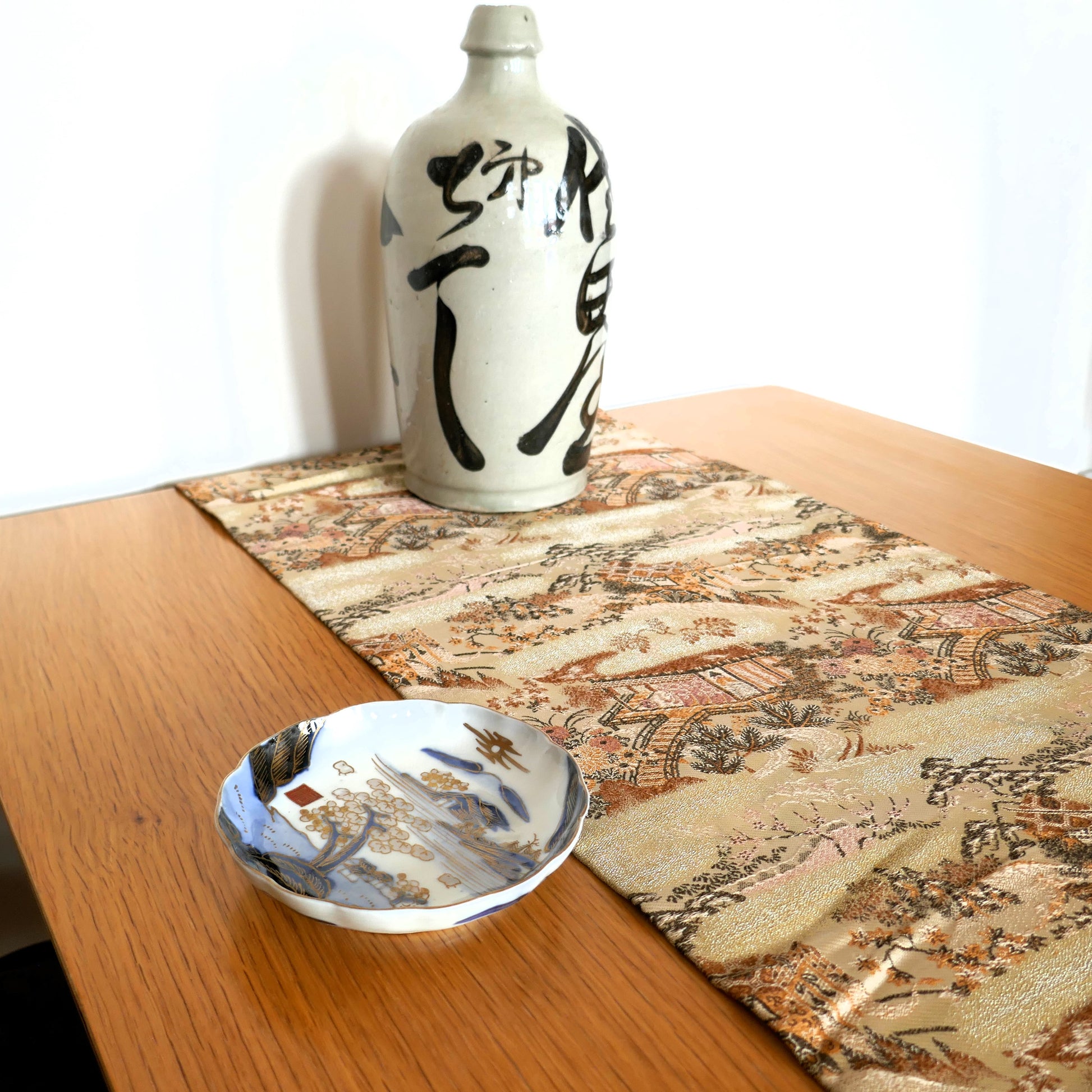 mise en scène d'une table avec une déco japonaise composée d'un maru obi en chemin de table d'une tokkuri et d'une assiette japonaise ancienne