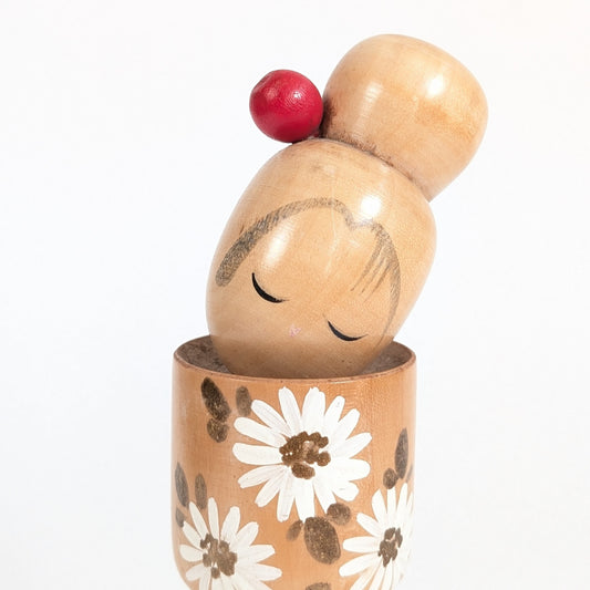 Détail du visage peint d’une kokeshi Ishida Tomio, yeux fermés, tête inclinée et chignon orné de rouge.