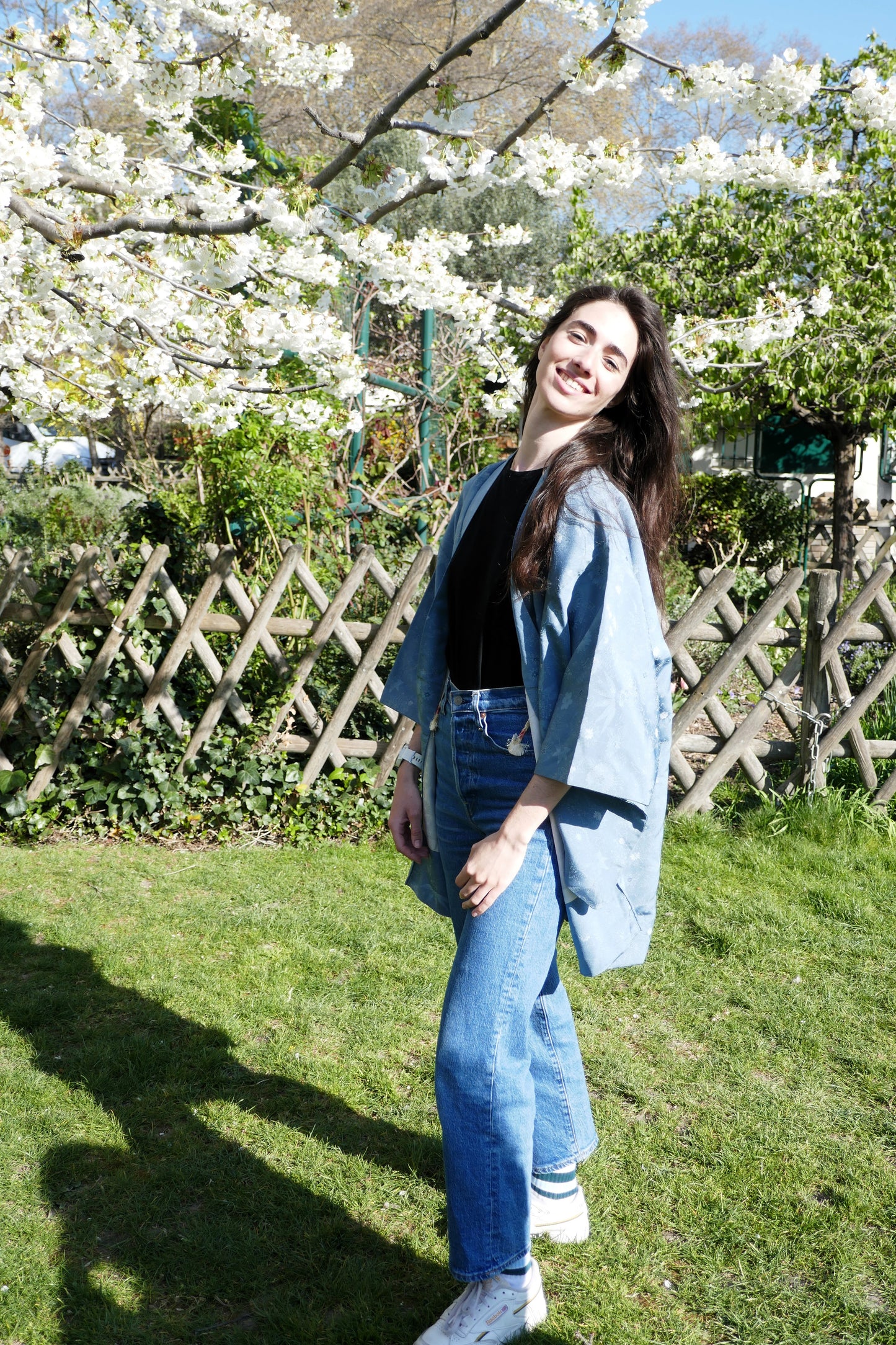Haori bleu en soie porté par Mayssa, vue de face sous un cerisier en fleurs.