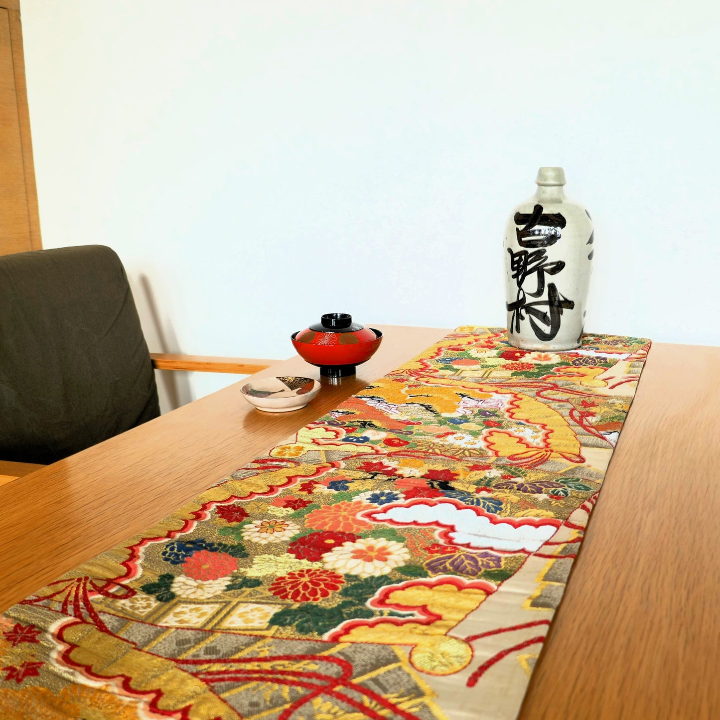 mise en scène du table à l'ambiance japonaise avec un maru obi en chemin de table et une tokkuri au fond un bol en laque et une coupelle ceramique