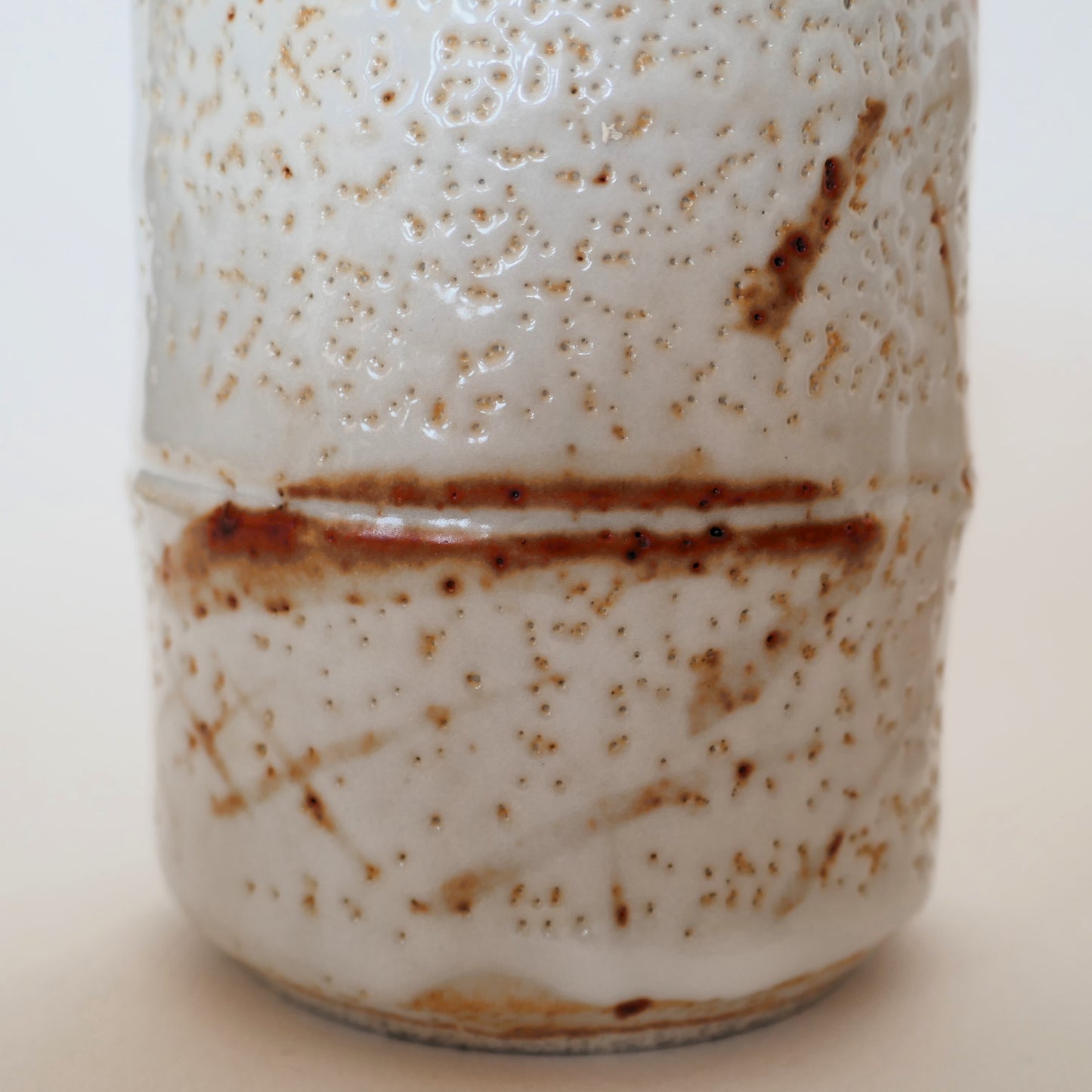 Zoom sur la surface d’une tasse japonaise Shino-yaki montrant la glaçure à effet de neige et les motifs brun rouge.