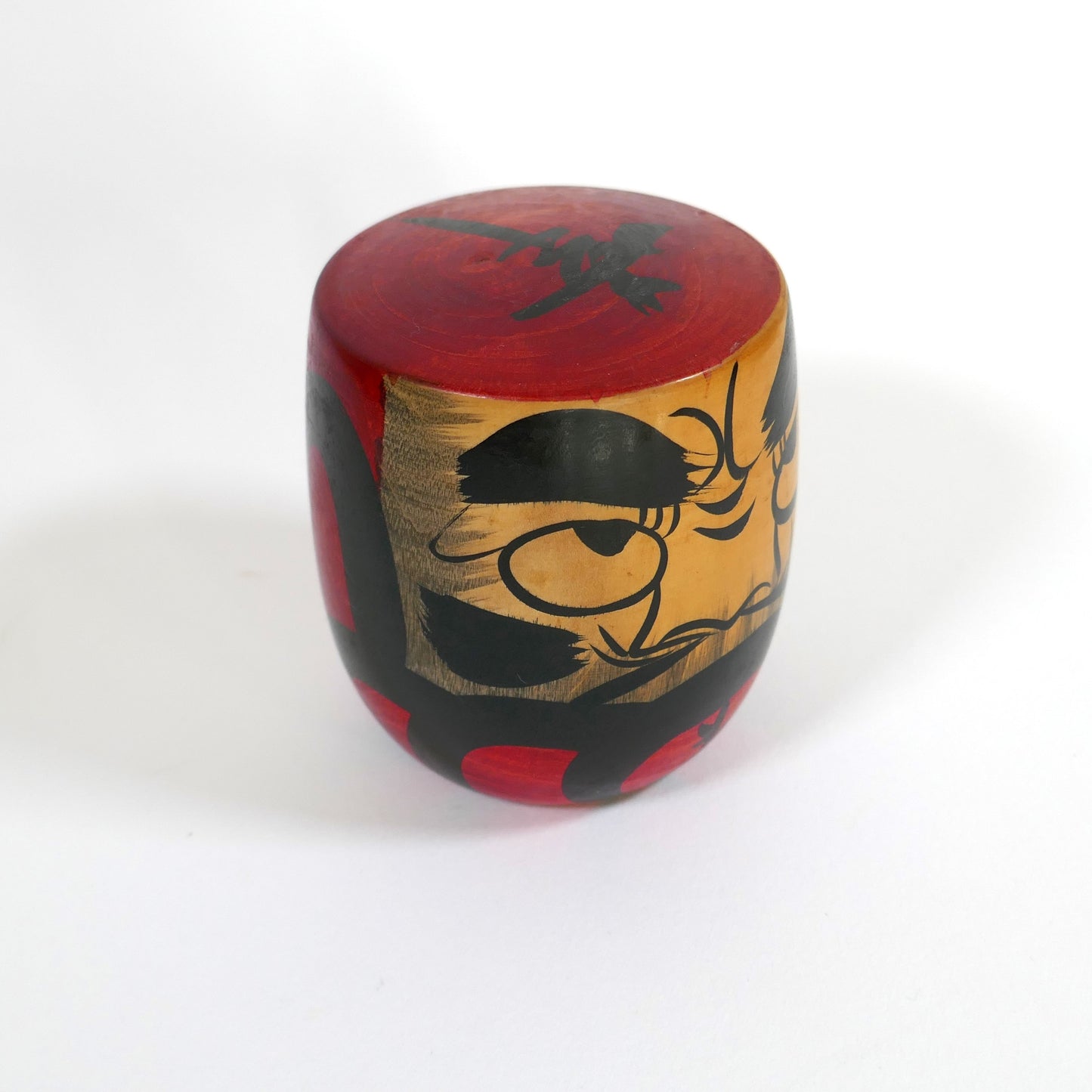 Profil d’une kokeshi Daruma artisanale au regard intense et peinture brossée