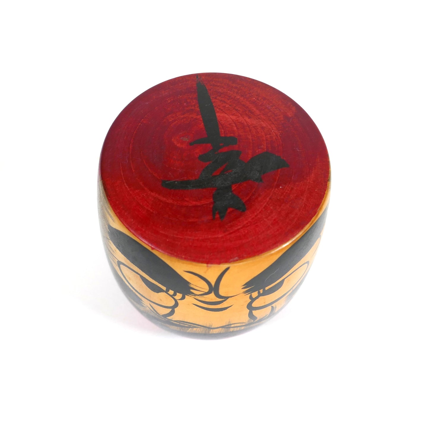 Vue du dessus d’une kokeshi Daruma, avec kanji noir sur fond rouge peint