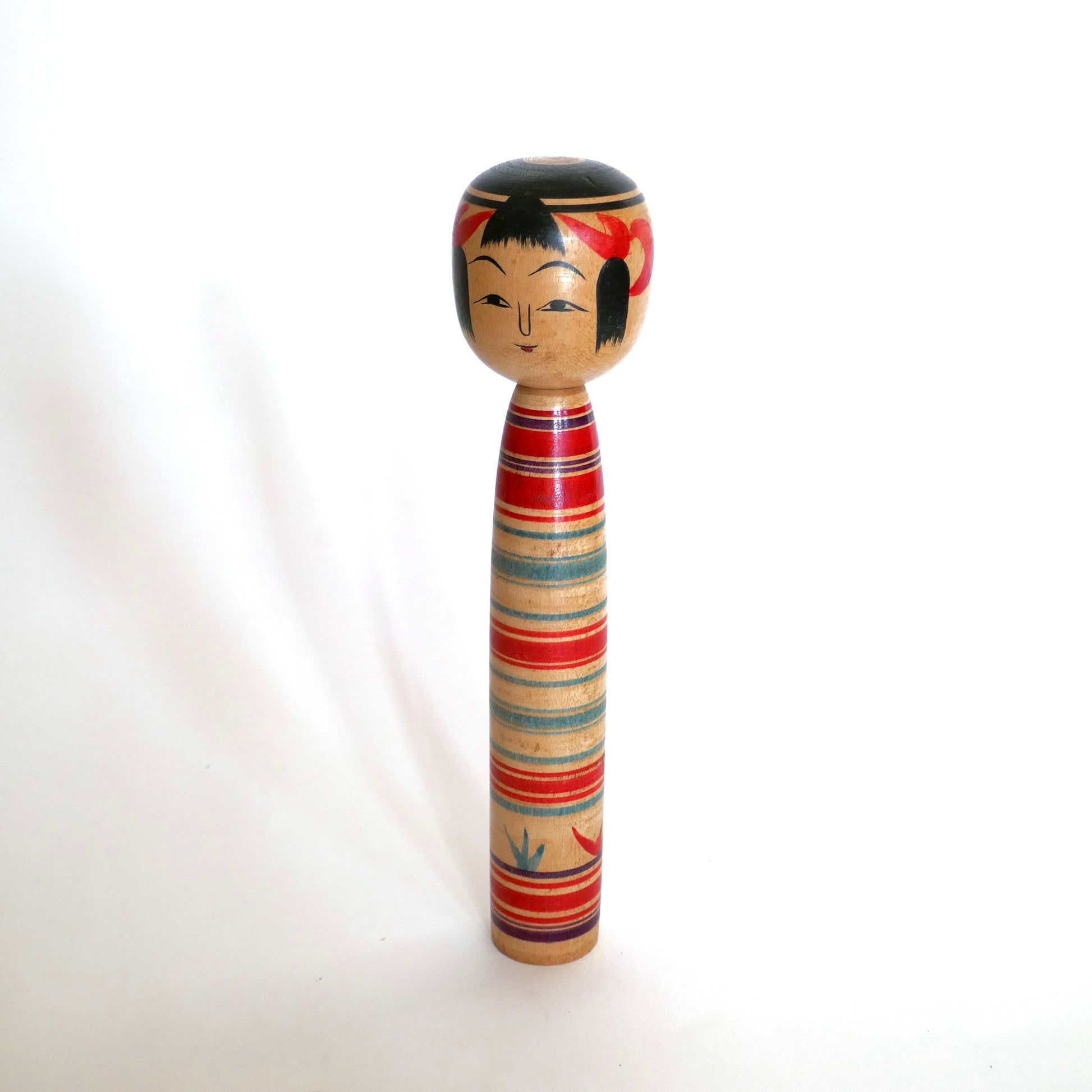 Kokeshi traditionnelle japonaise Tsuchiyu vue en trois-quarts face, réalisée par Watanabe Sadami en 1969. Œuvre artisanale en bois, peinte à la main avec des motifs rouges et bleus typiques de l’école Tsuchiyu.