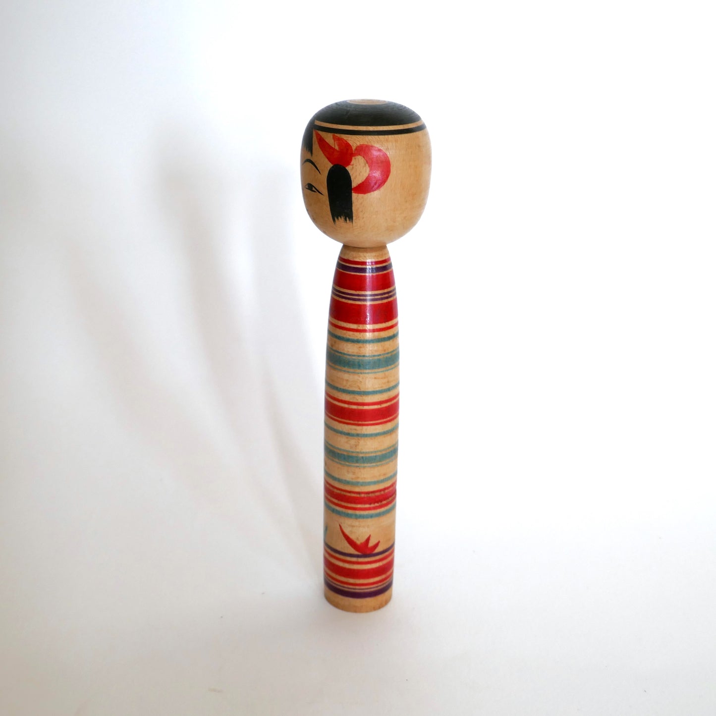 Profil gauche d’une kokeshi japonaise traditionnelle signée Watanabe Sadami, maître du style Tsuchiyu. Peinture manuelle aux couleurs vives, typique des poupées artisanales de la période Shōwa.