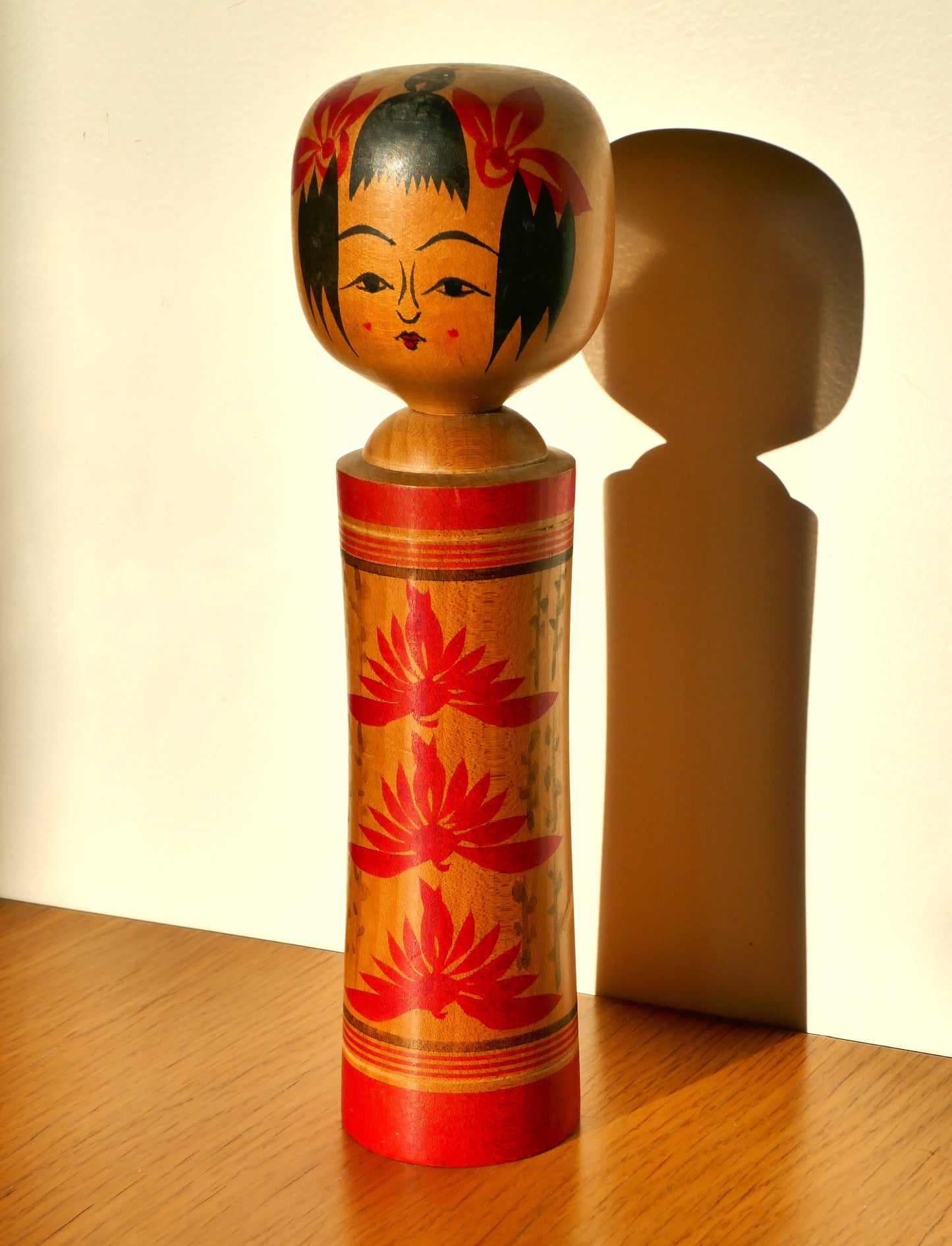 Kokeshi Naruko éclairée par la lumière naturelle, mettant en valeur les couleurs vives.