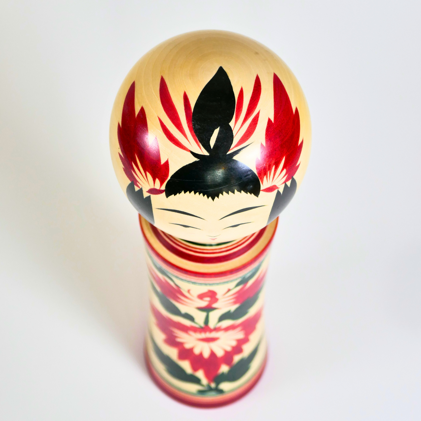 Vue du dessus d’une kokeshi Naruko avec coiffure noire et détails rouges