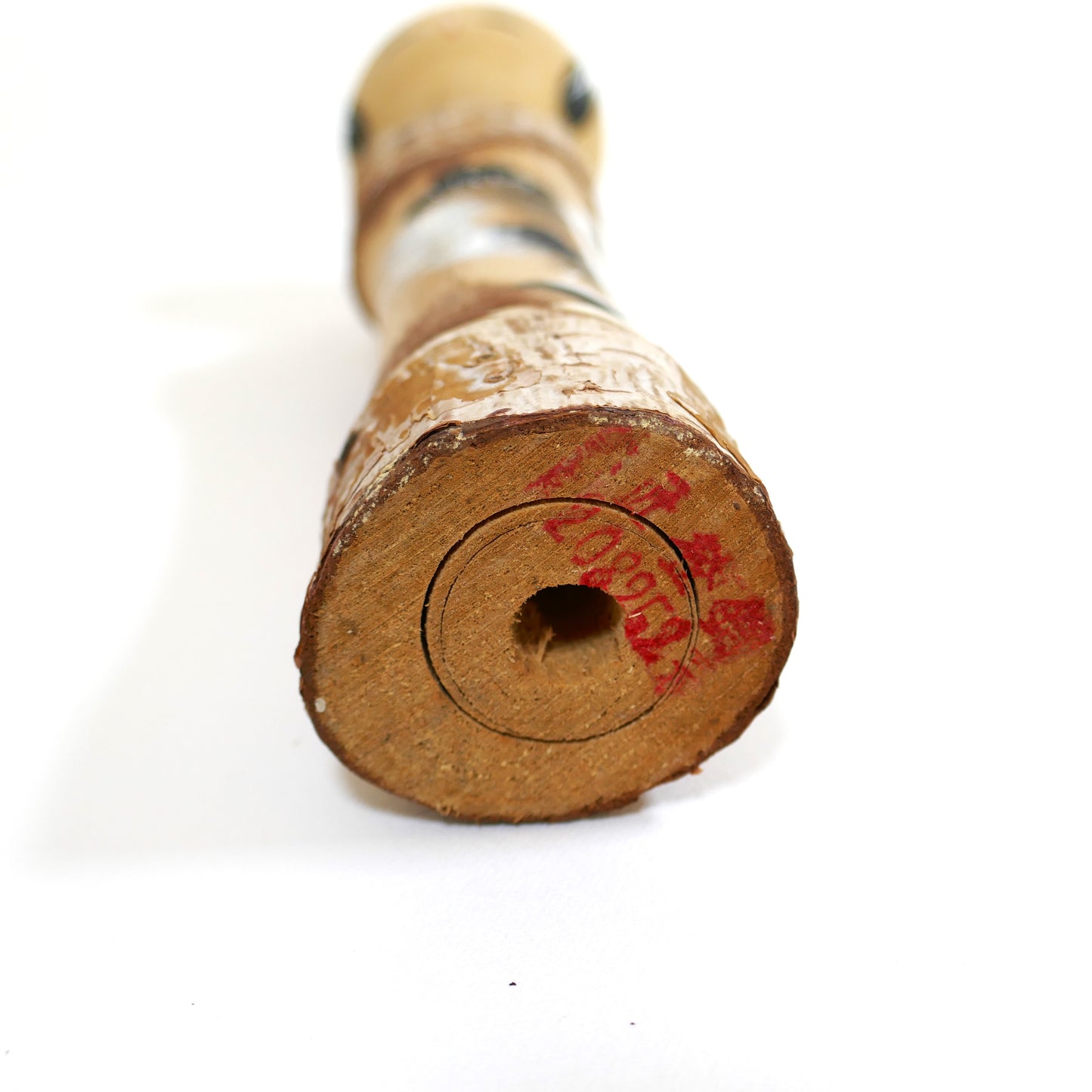 Base estampillée d'une kokeshi omiyage de Nikkō avec marquage rouge illisible.