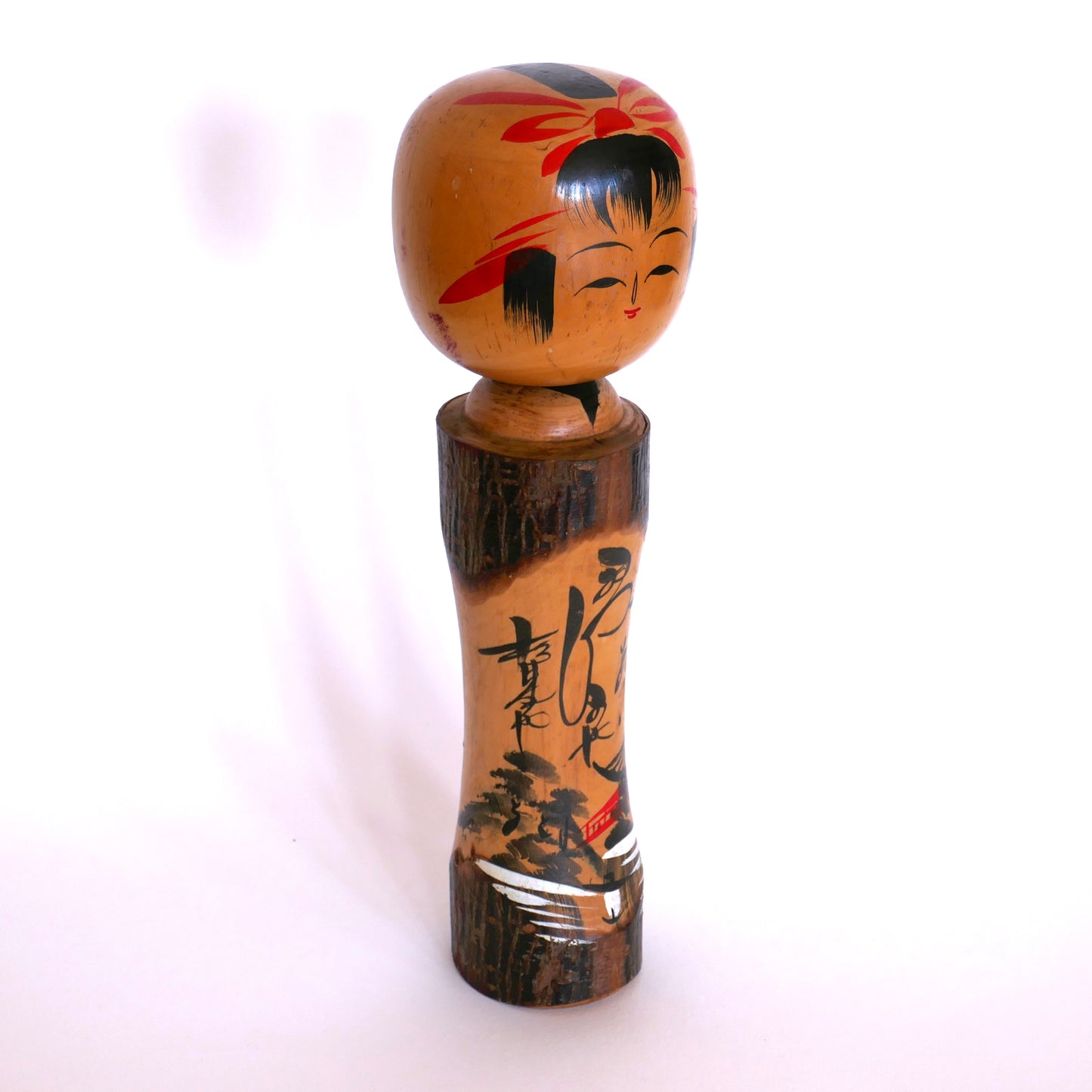 Vue de trois quart droit d’une kokeshi omiyage ancienne – décor montagnard peint et signature calligraphiée de l’artisan Iwasaki