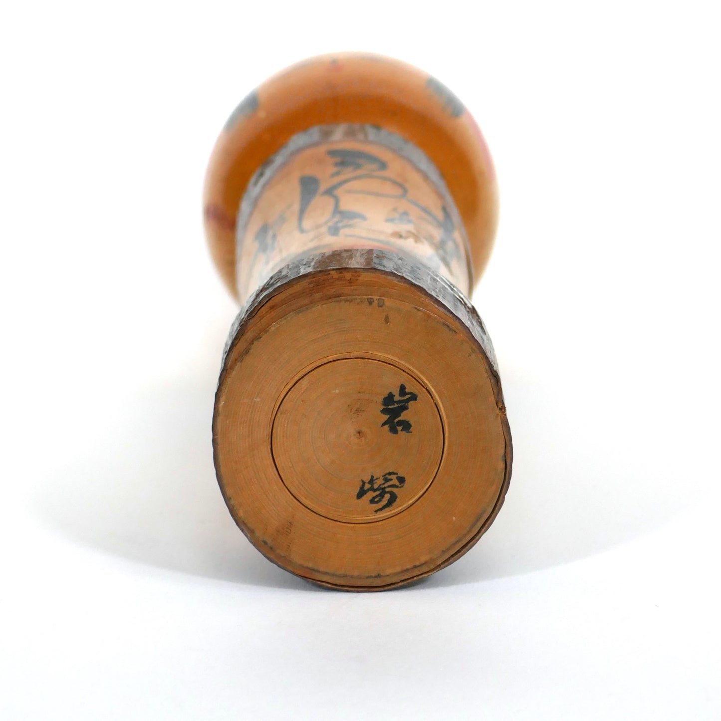 Signature calligraphiée de l’artisan Iwasaki (岩崎) sous une kokeshi souvenir japonaise – bois tourné et gravure à l’encre noire