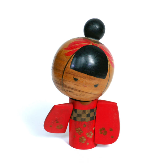 Kokeshi japonaise ancienne de Sansaku Sekiguchi avec kimono rouge à fleurs et chignon noir.