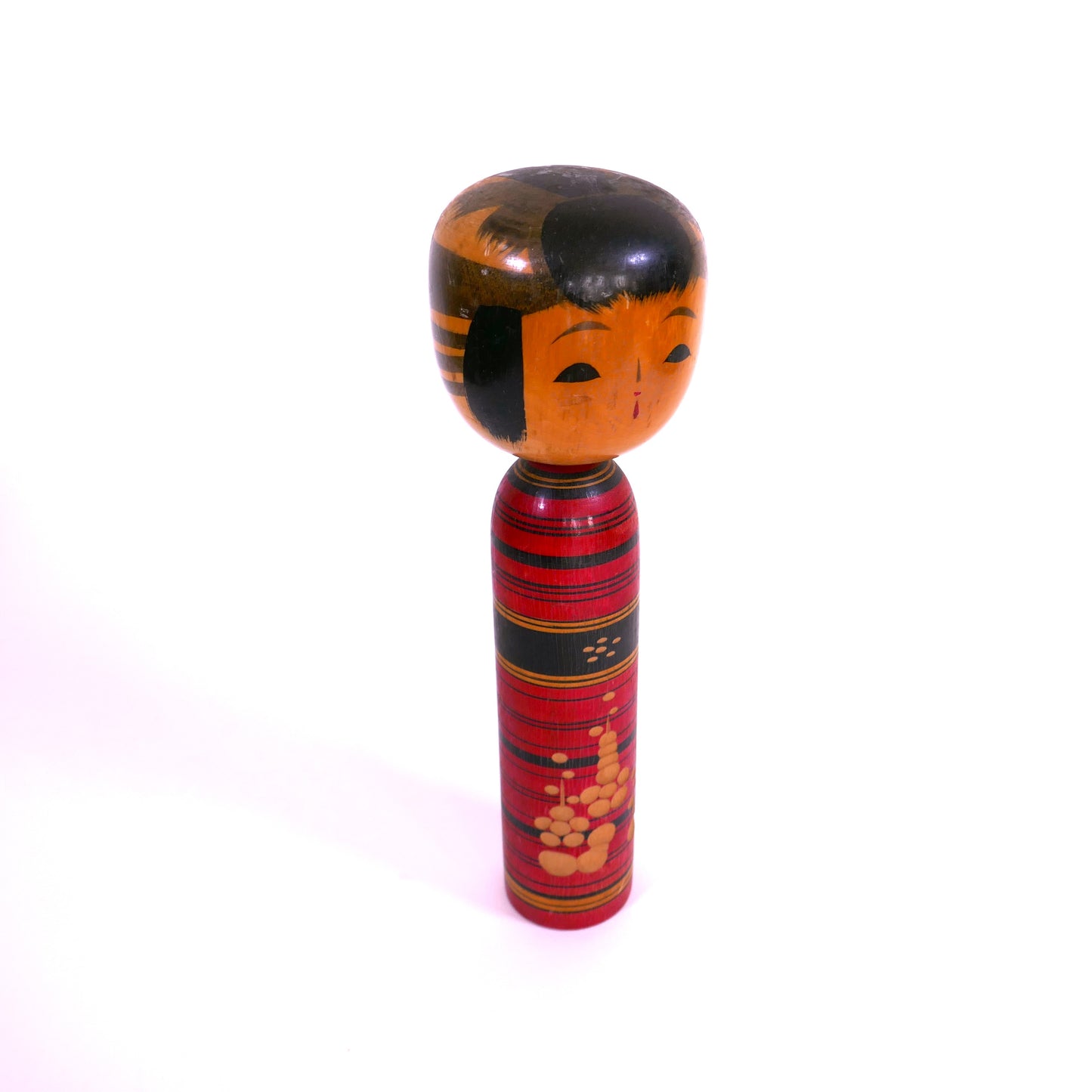 Kokeshi vintage shingata en bois peint rouge et noir, expression douce, vue en angle.
