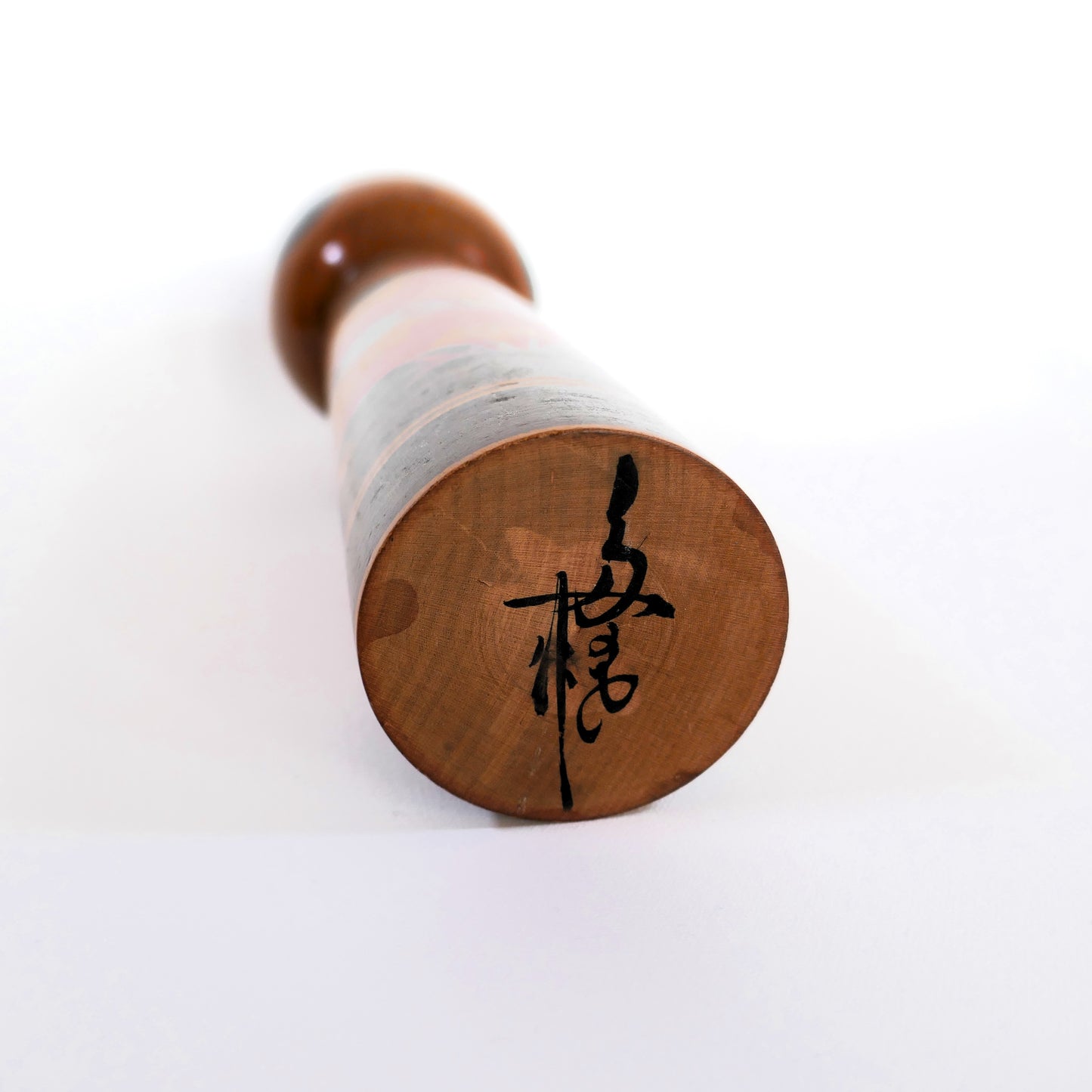 Signature de l'artisan Kiyohara Takao sous une kokeshi japonaise Shingata décorée de camélias.