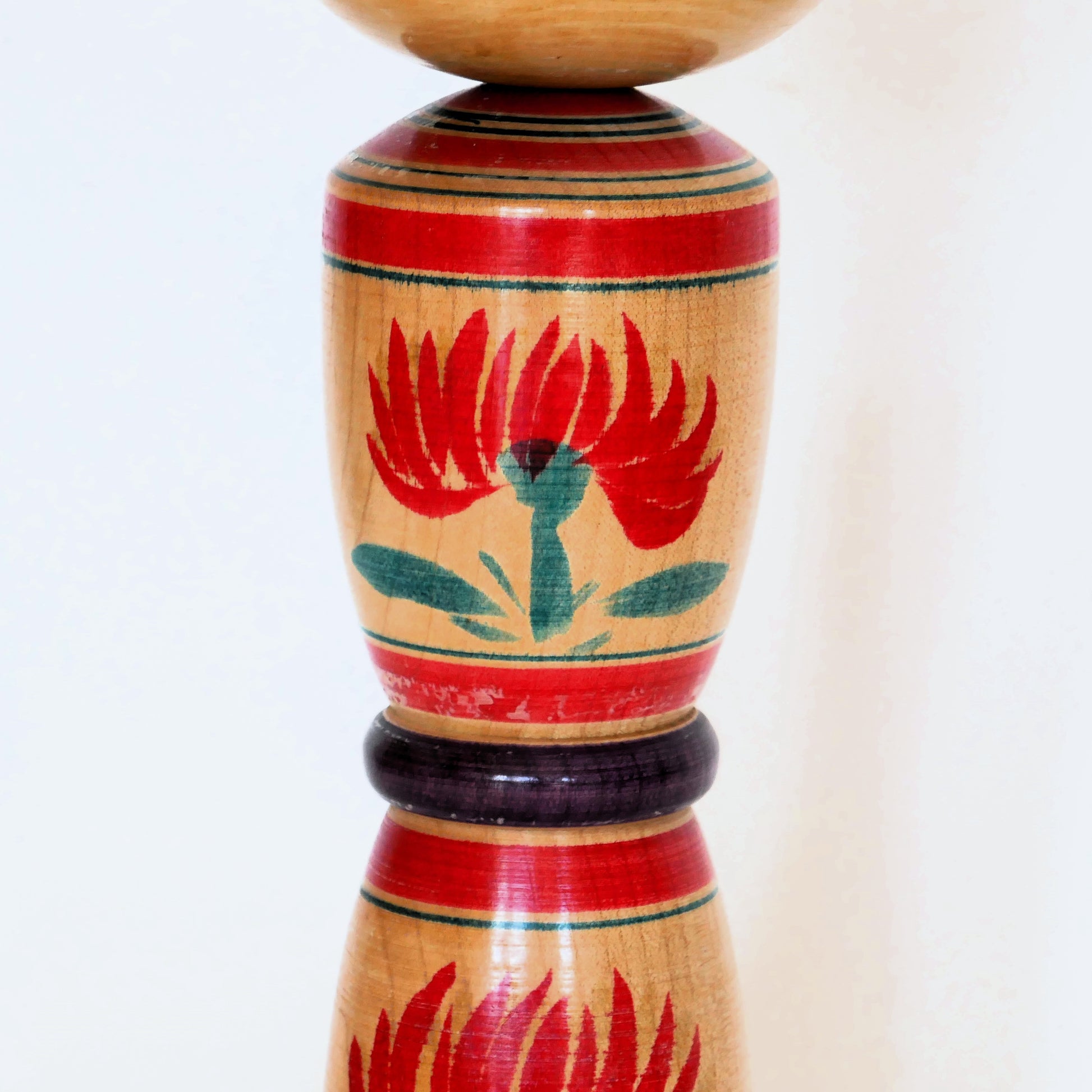 Détail en zoom des fleurs peintes sur le corps d'une kokeshi shingata de style Yajirō