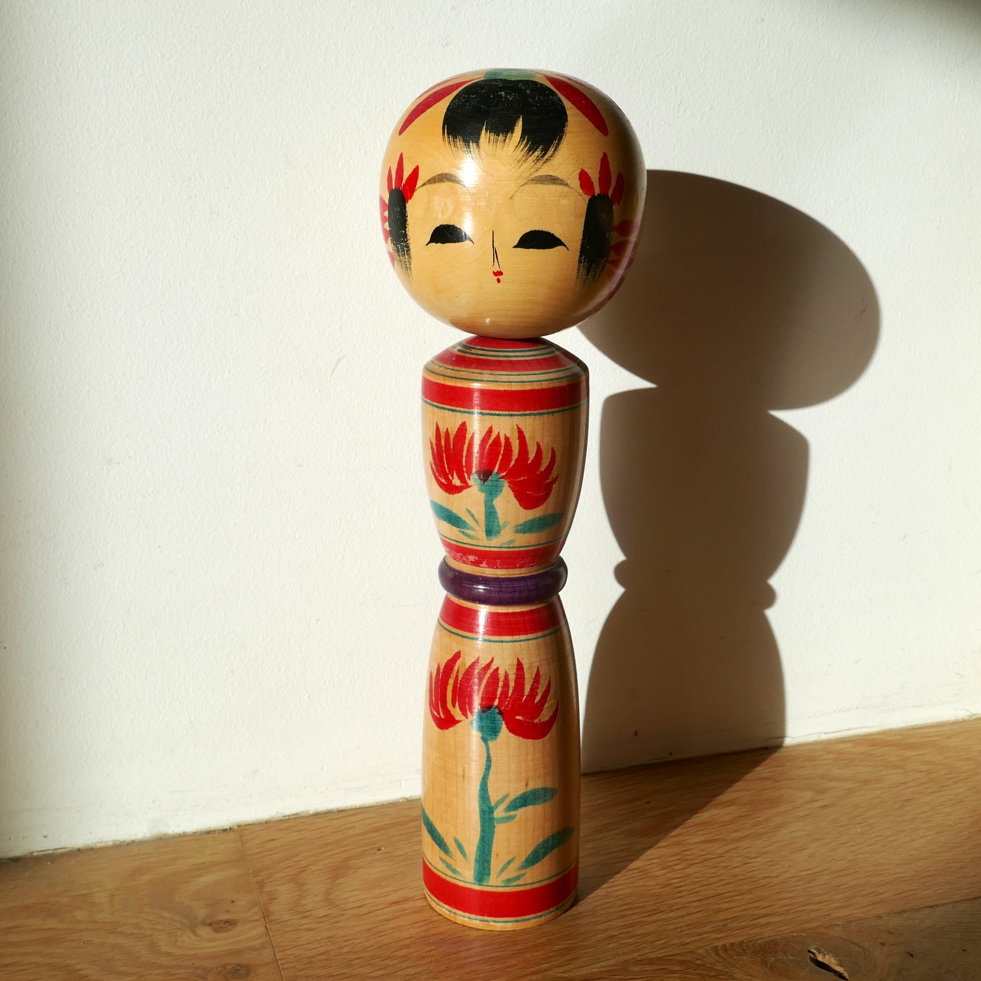 Mise en scène de la kokeshi shingata par Yanome Hachizô, sous une lumière naturelle posée sur un parquet bois et fond blanc