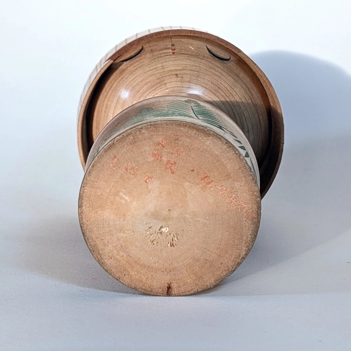 Photo du dessous de la kokeshi sōsaku signée Ueda Izumi, base en bois naturel, artisanat japonais.