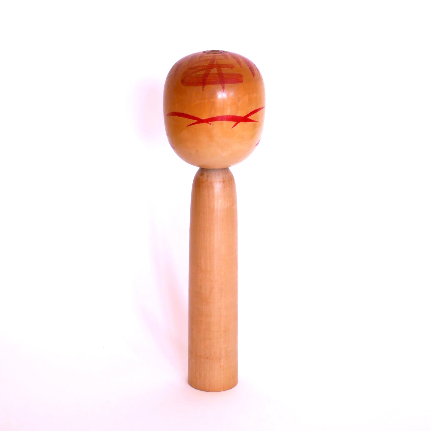 Vue de dos d’une poupée kokeshi Togatta – tête peinte avec motifs solaires rouges typiques de Satō Kesakichi