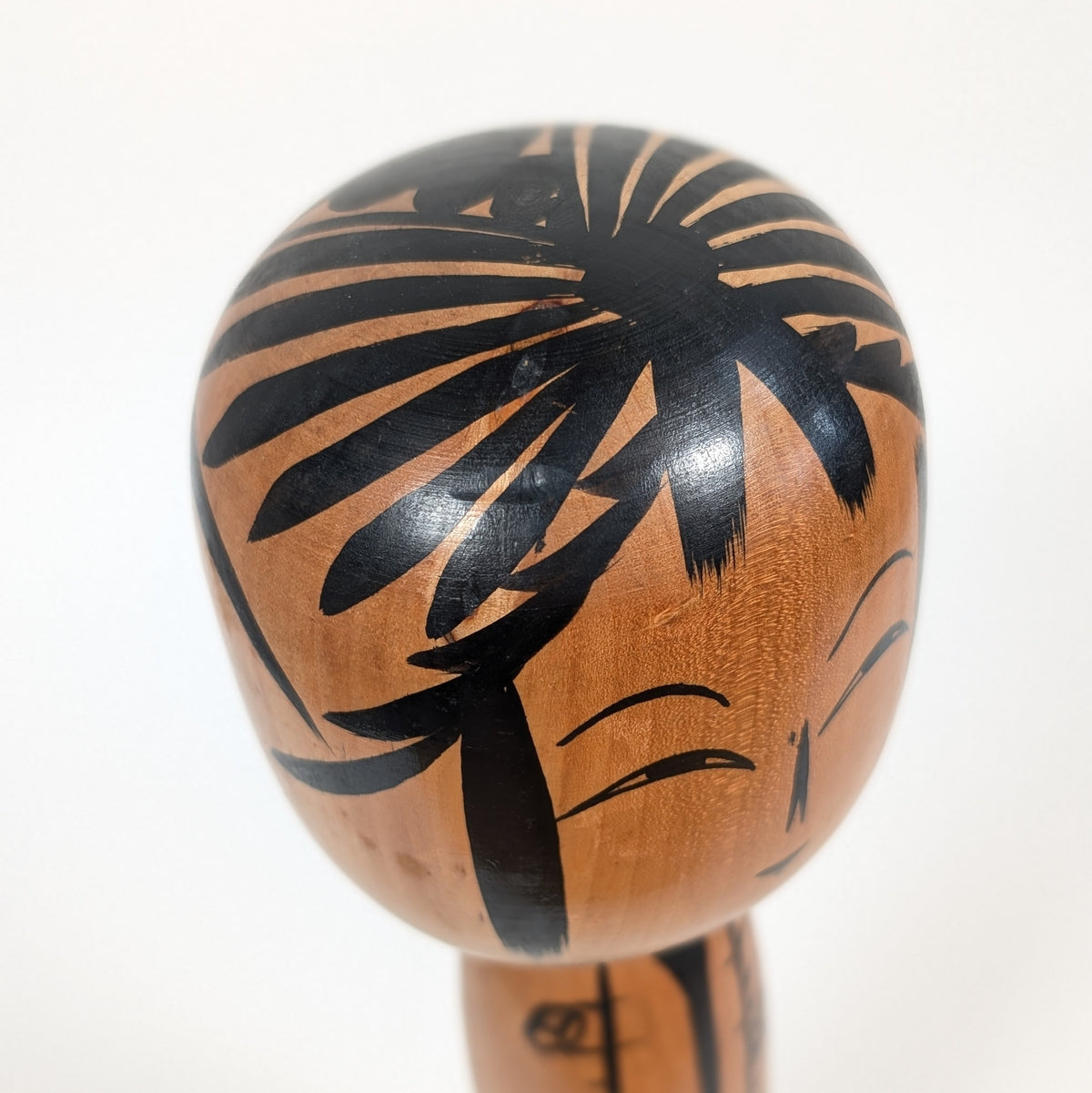 Gros plan du visage souriant d'une dentō kokeshi Tōgatta, aux yeux futae-mabuta, au nez ware-bana et aux cheveux noirs.
