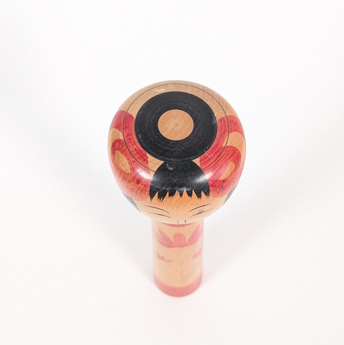 Motif janome 蛇の目 sur la tête d’une kokeshi Tsuchiyu, décor œil de serpent et coiffure noire stylisée