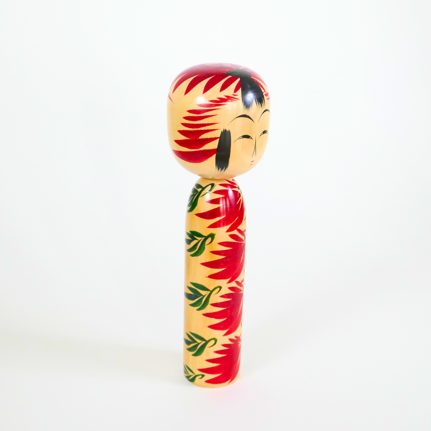 une poupée kokeshi en bois de style hijiori yamagata signée Kobayashi Shozo vue de trois quarts rouge et verte