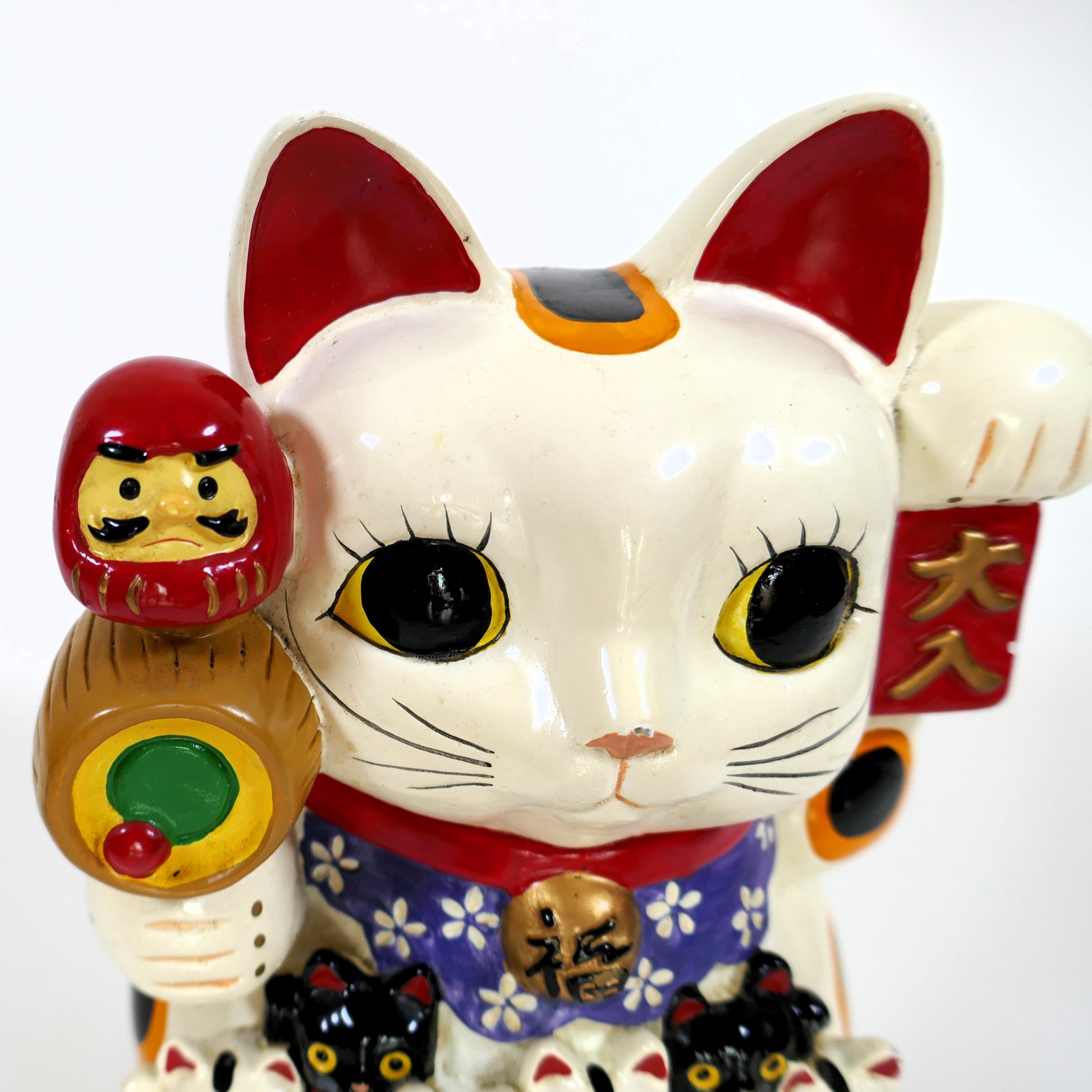 Gros plan sur le visage du maneki neko et son tambour avec daruma porte-bonheur